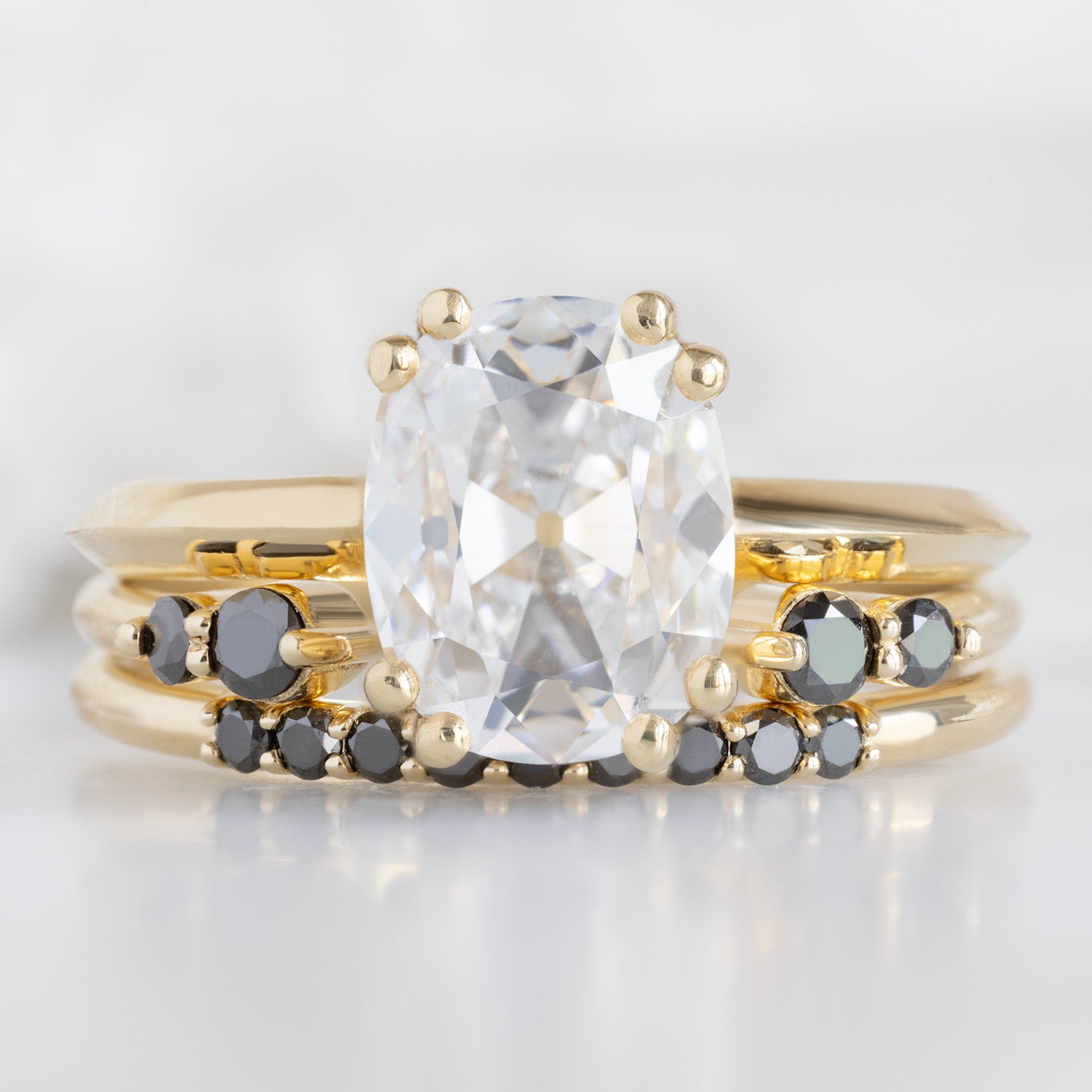 The Luxe Black Diamond Pavé Wedding Band in 14K Yellow Gold Stacked with White Diamond Cushion Cut Engagement Ring on White Marble