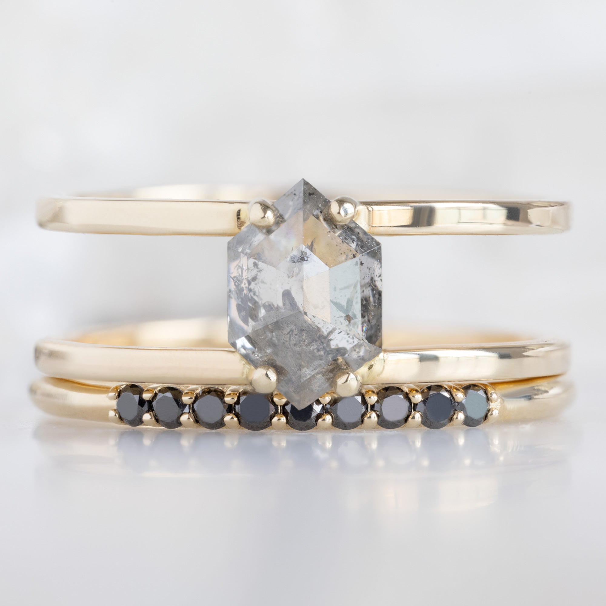 The Luxe Black Diamond Pavé Wedding Band in 14K Yellow Gold Stacked with Double Band Salt and Pepper Diamond Engagement Ring on White Marble