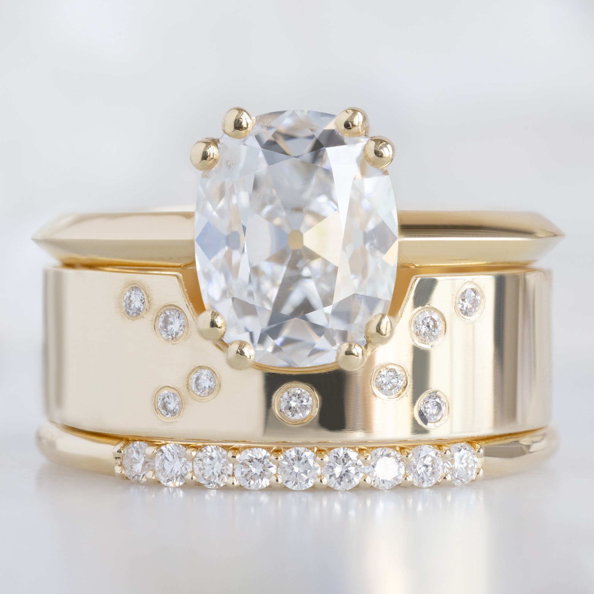 The Luxe White Diamond Pavé Wedding Band in 14k Yellow Gold Stacked with White Diamond Cushion-Cut Engagement Ring on White Marble