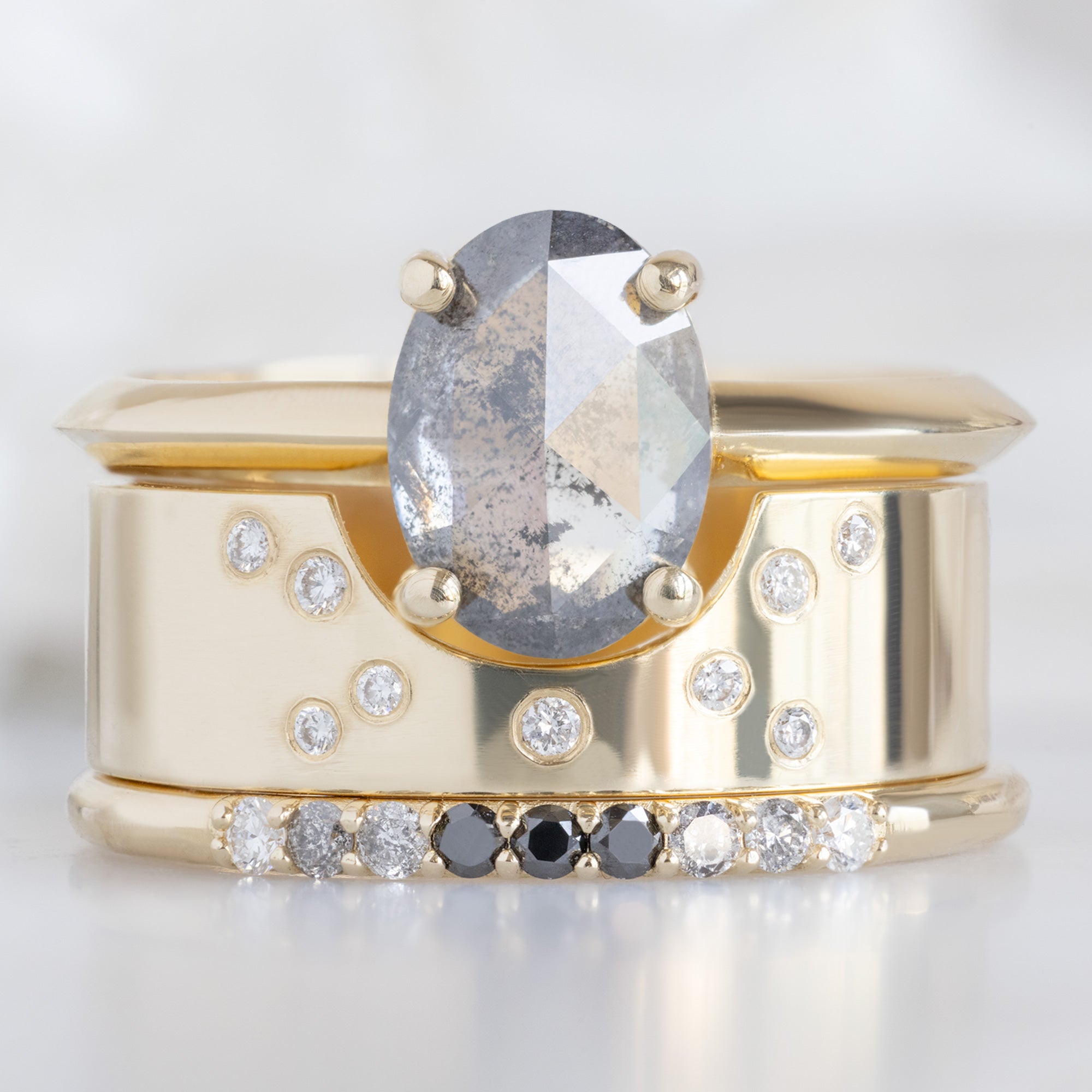 The Luxe Ombré Diamond Pavé Wedding Band in 14K Yellow Gold Stacked with Oval Salt and Pepper Diamond Engagement Ring on White Marble