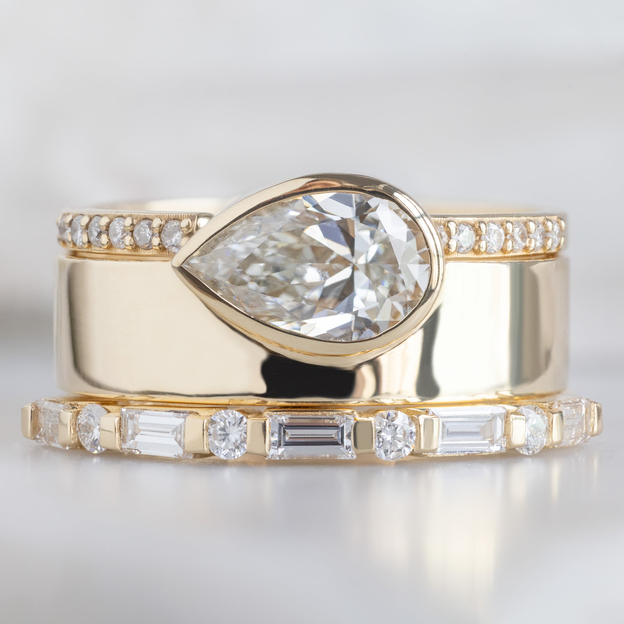 The Luxe Baguette White Diamond Eternity Band in 14K Yellow Gold stacked with cigar band white diamond engagement ring on white marble surface