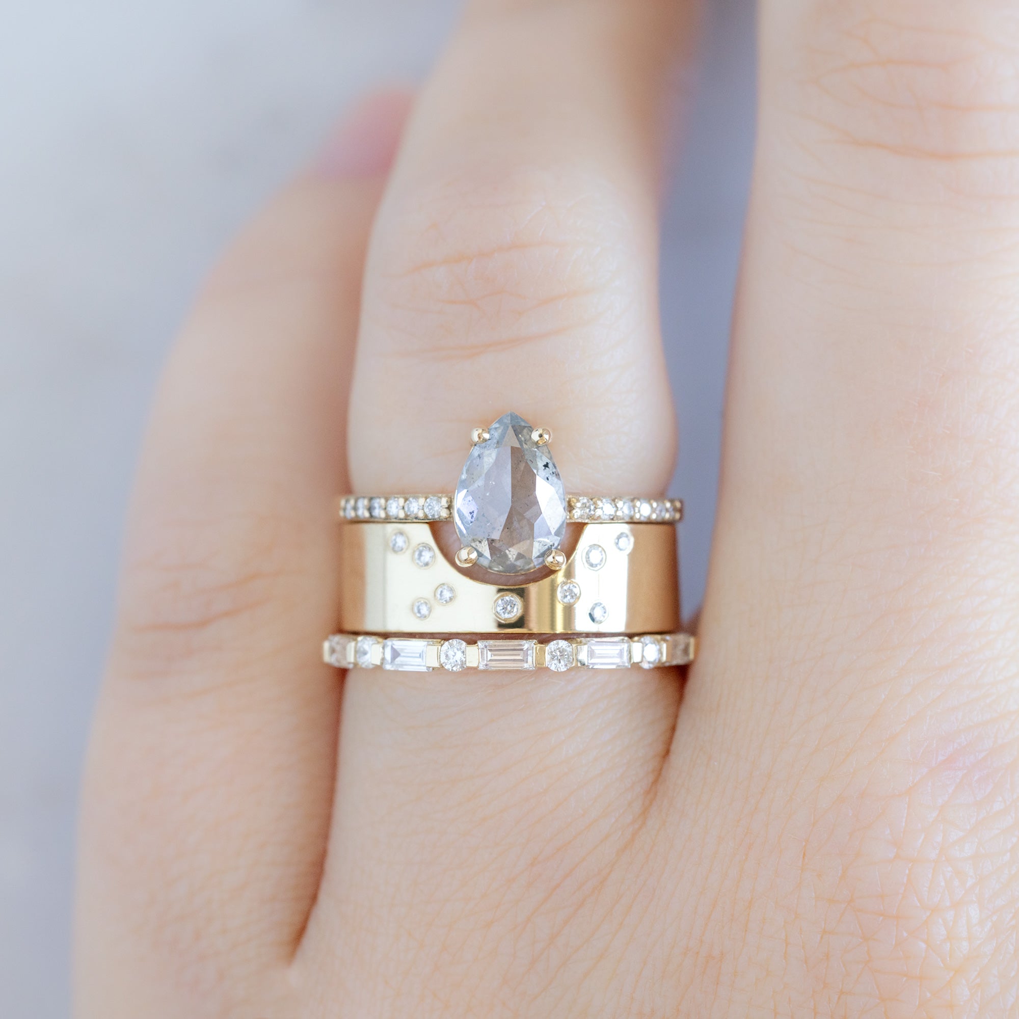 The Luxe Baguette White Diamond Eternity Band in 14K Yellow Gold stacked with salt and pepper pear diamond engagement ring on model