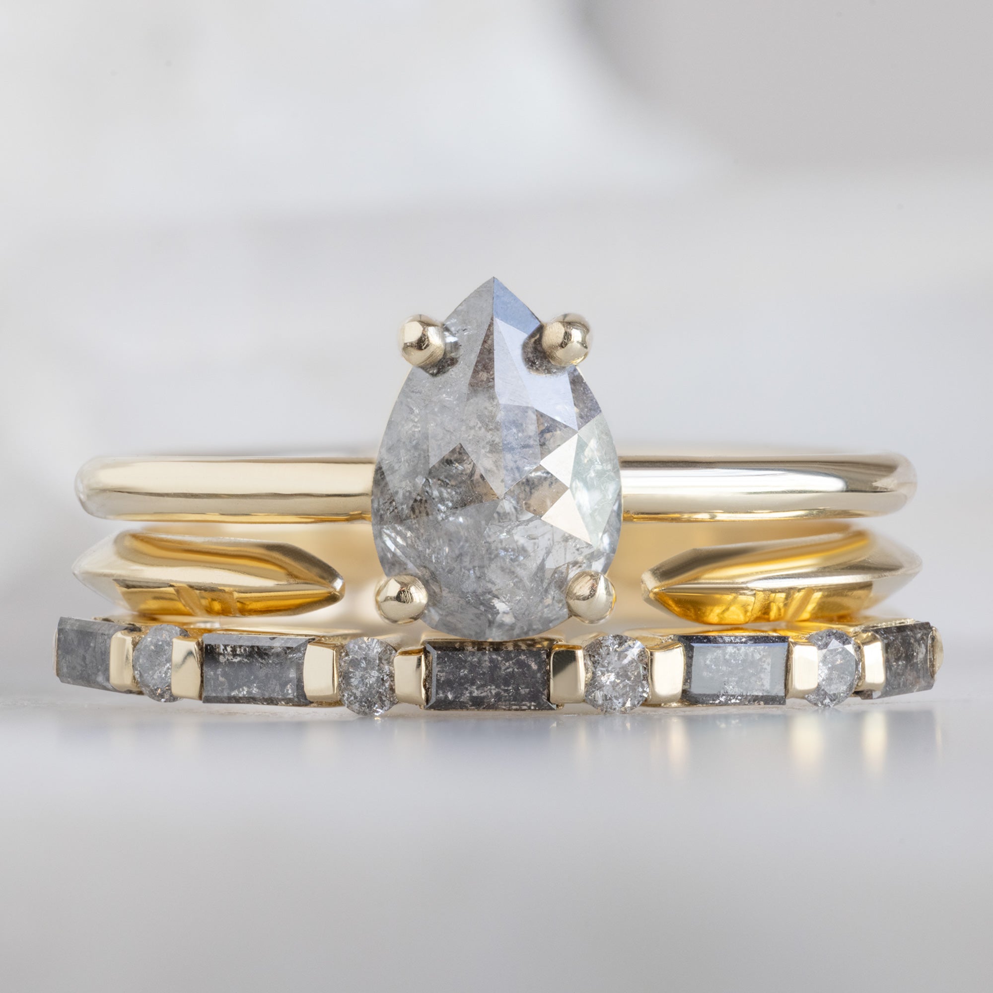 The Luxe Baguette Salt and Pepper Diamond Eternity Band in 14K Rose Gold stacked with pear salt and pepper diamond engagement ring on white marble surface