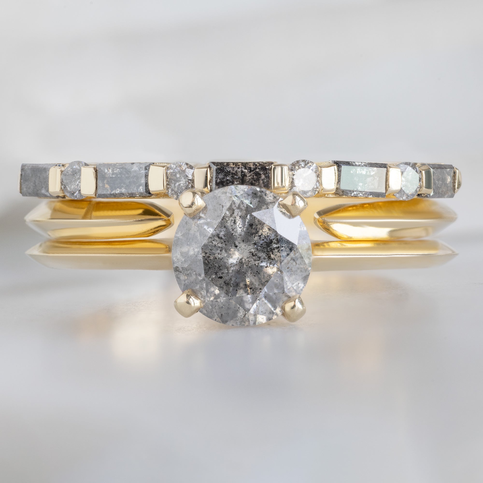 The Luxe Baguette Salt and Pepper Diamond Eternity Band in 14K Rose Gold stacked with round salt and pepper diamond engagement ring on white marble surface