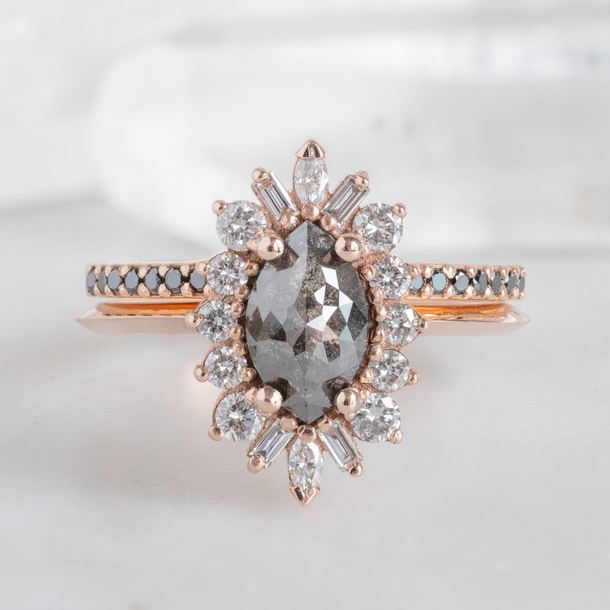 The Black Diamond Pavé Wedding Band in 14K Rose Gold Stacked with Black Marquise Diamond Engagement Ring on White Marble Tile