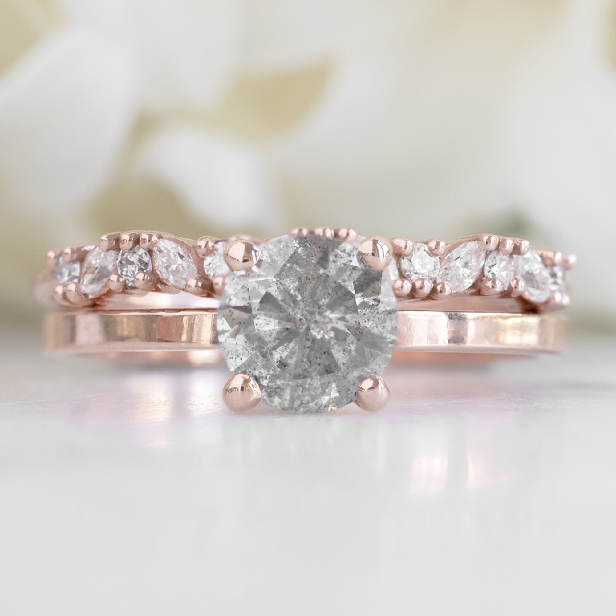 The Marquise Confetti Wedding Band in 14K Rose Gold Stacked with Round Salt and Pepper Diamond Engagement Ring on White Marble Tile