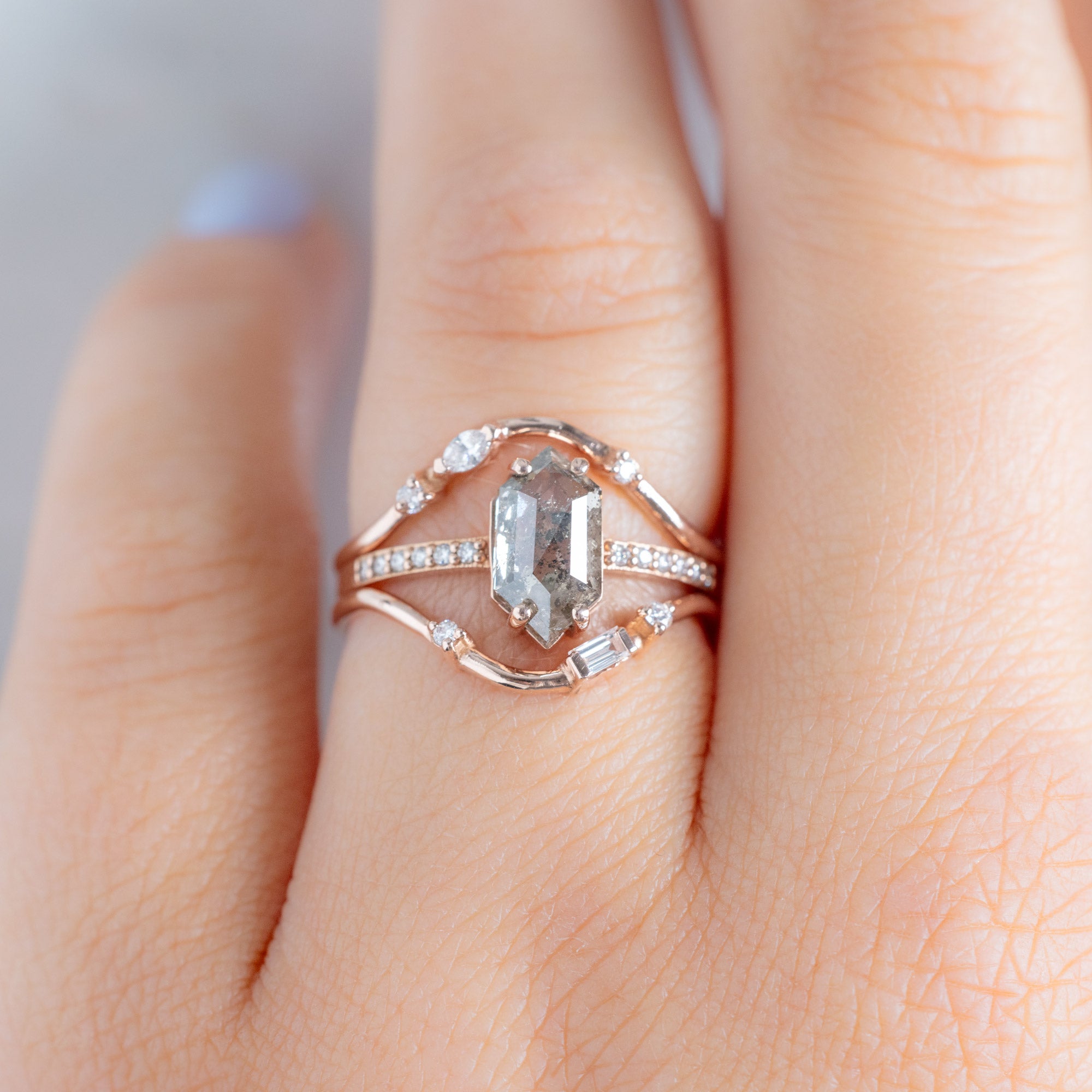 Asymmetrical Baguette Diamond Arc Stacking Band in 14K Rose Gold on White Marble Stacked with a Salt and Pepper Diamond Hexagon Engagement Ring on Model
