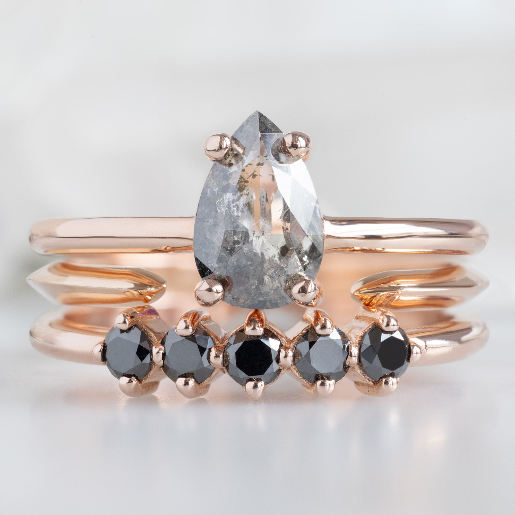 The Sequent Black Diamond Wedding Band in 14K Rose Gold Stacked with Peak Salt and Pepper Diamond Engagement on White Marble