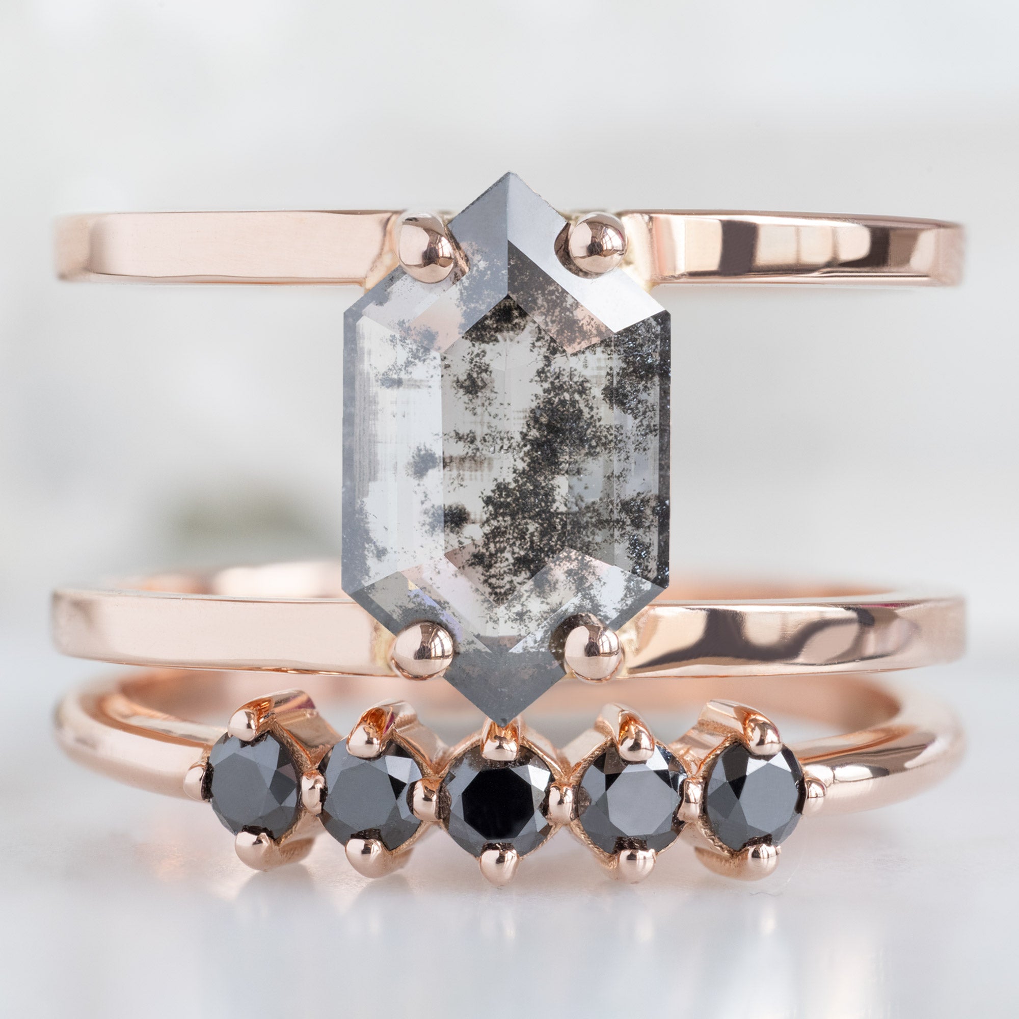 The Sequent Black Diamond Wedding Band in 14K Rose Gold Stacked with Double Band Salt and Pepper Diamond Engagement Ring on White Marble