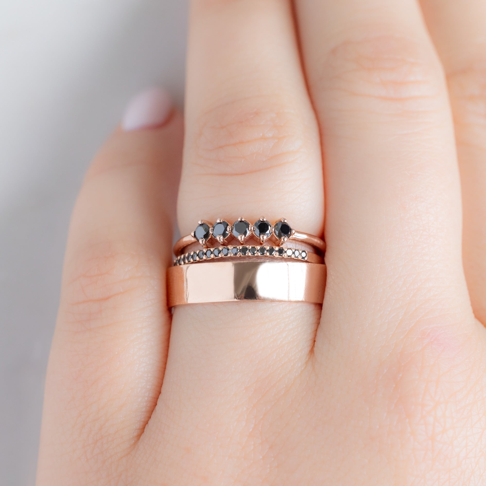 The Sequent Black Diamond Wedding Band in 14K Rose Gold Stacked with Fine Jewelry Rings on Model