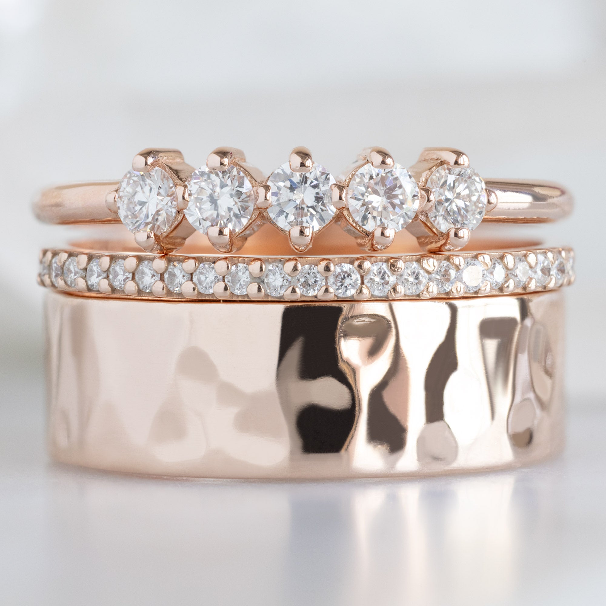 The Sequent White Diamond Wedding Band in 14K Rose Gold Stacked with Rose Gold Wedding Bands on White Marbe