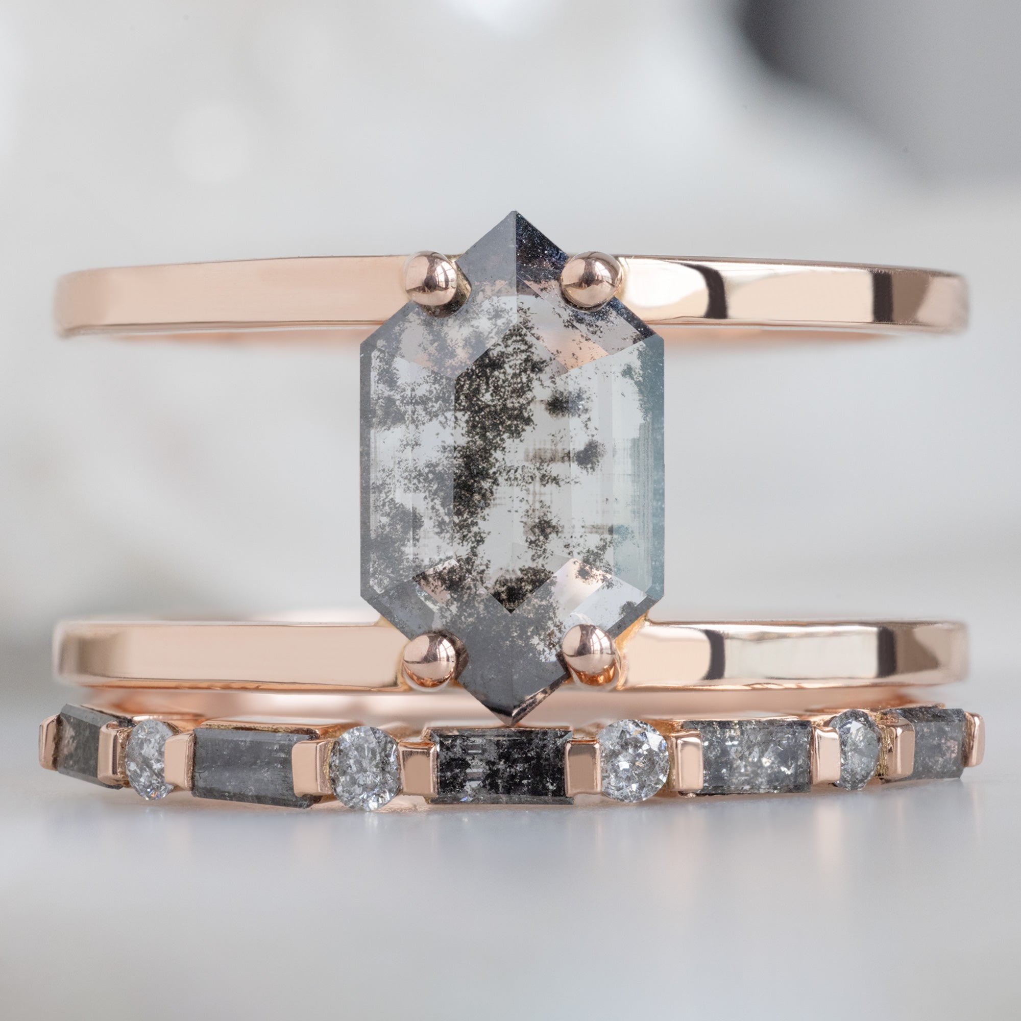 The Luxe Baguette Salt and Pepper Diamond Eternity Band in 14K Rose Gold  Stacked with a double banded hexagonal diamond engagement ring on White Marble Surface