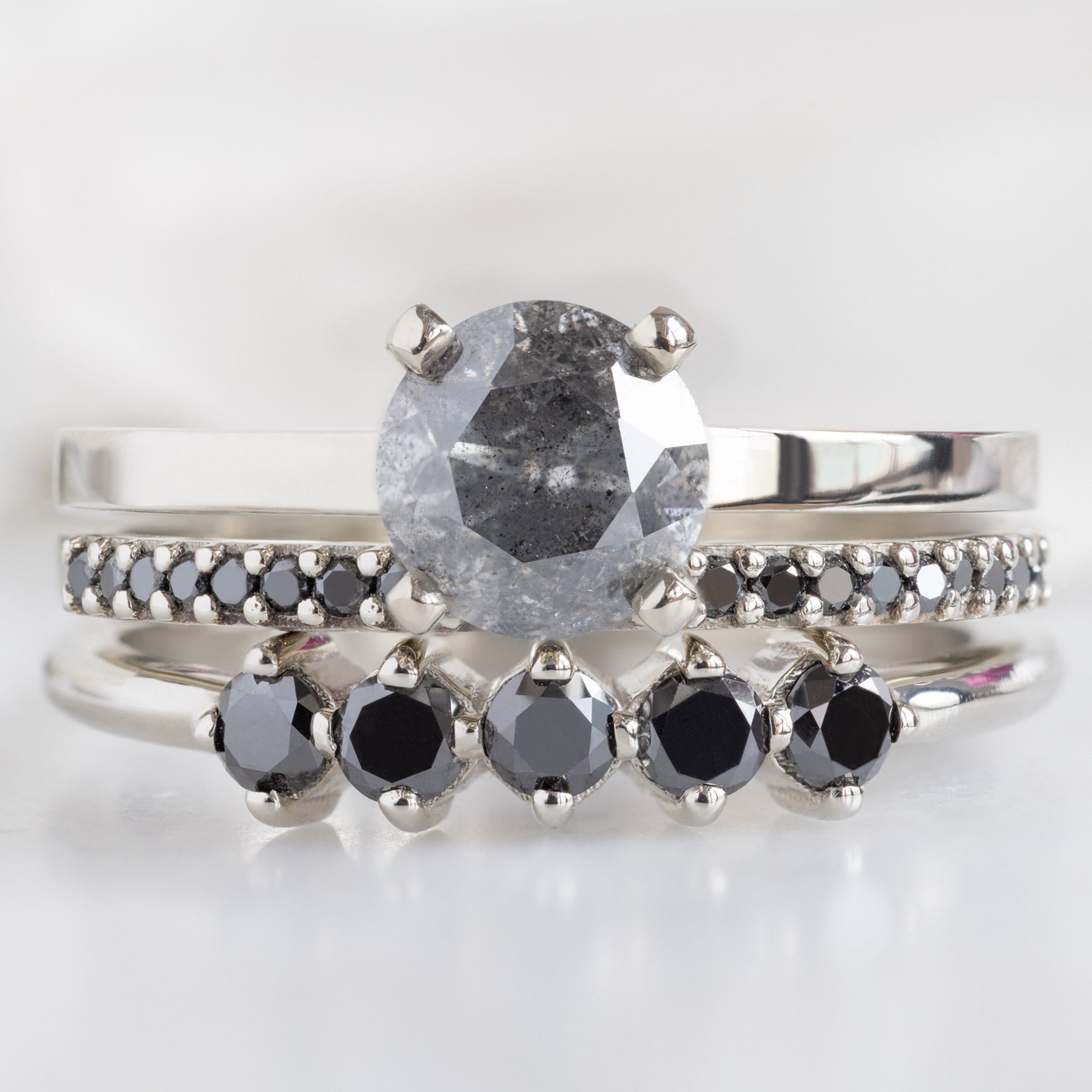 The Sequent Black Diamond Wedding Band in 14K White Gold Stacked with Round Salt and Pepper Diamond Engagement Ring on White Marble