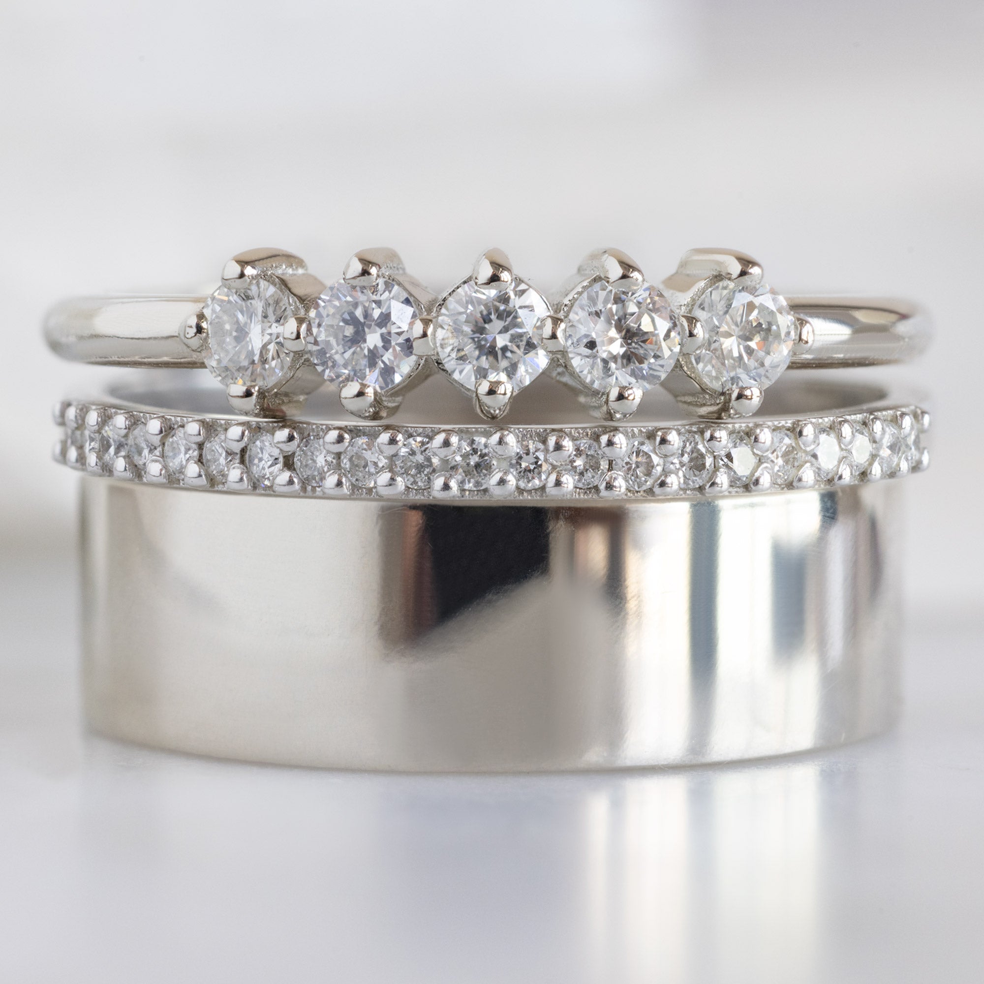 The Sequent White Diamond Wedding Band in 14K White Gold Stacked with White Gold Engagement Rings on White Marble