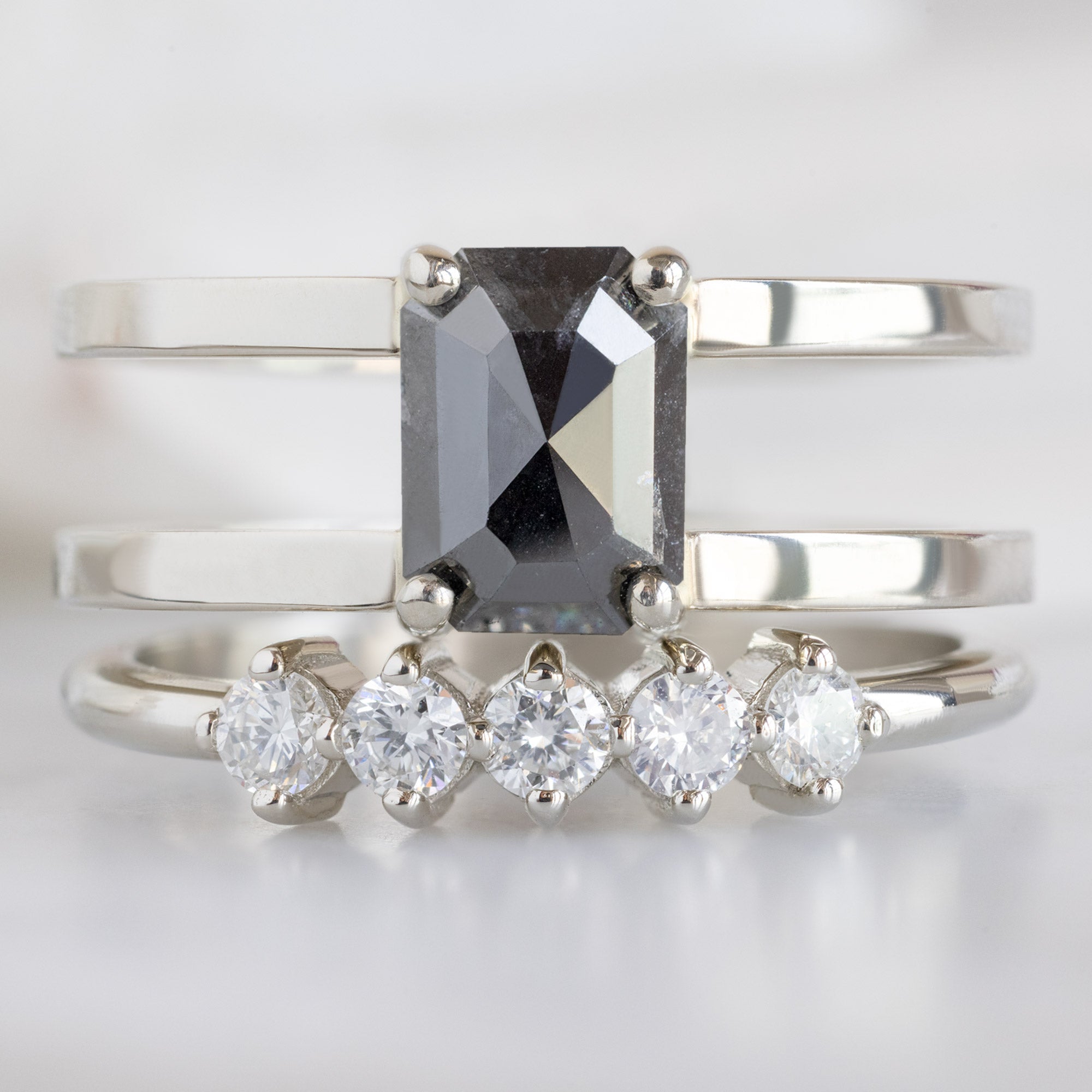 The Sequent White Diamond Wedding Band in 14K White Gold Stacked with Double Band Black Diamond Engagement Ring on White Marble