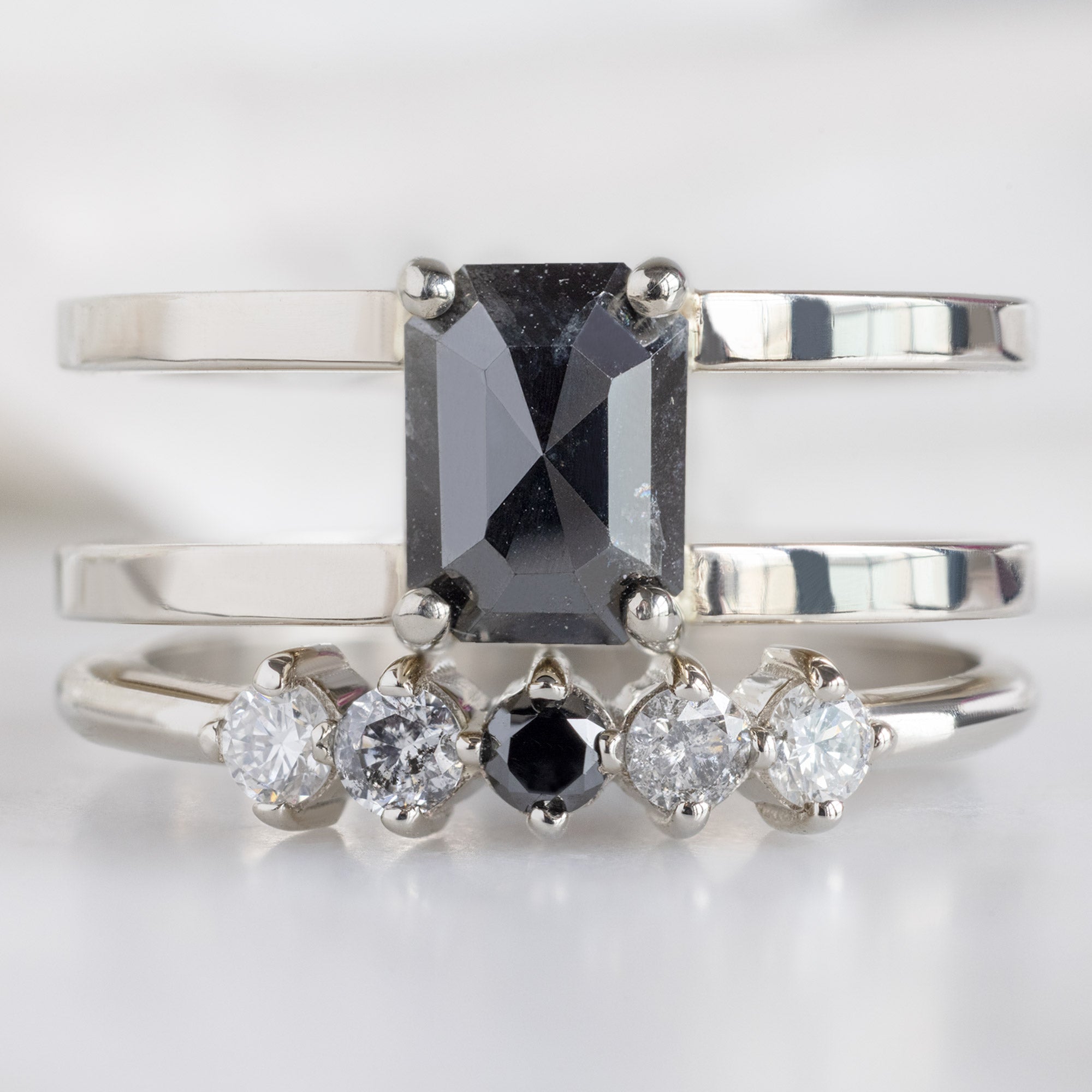 The Sequent Ombré Diamond Wedding Band in 14K White Gold Stacked with Double Band Black Diamond Engagement Ring on White Marble