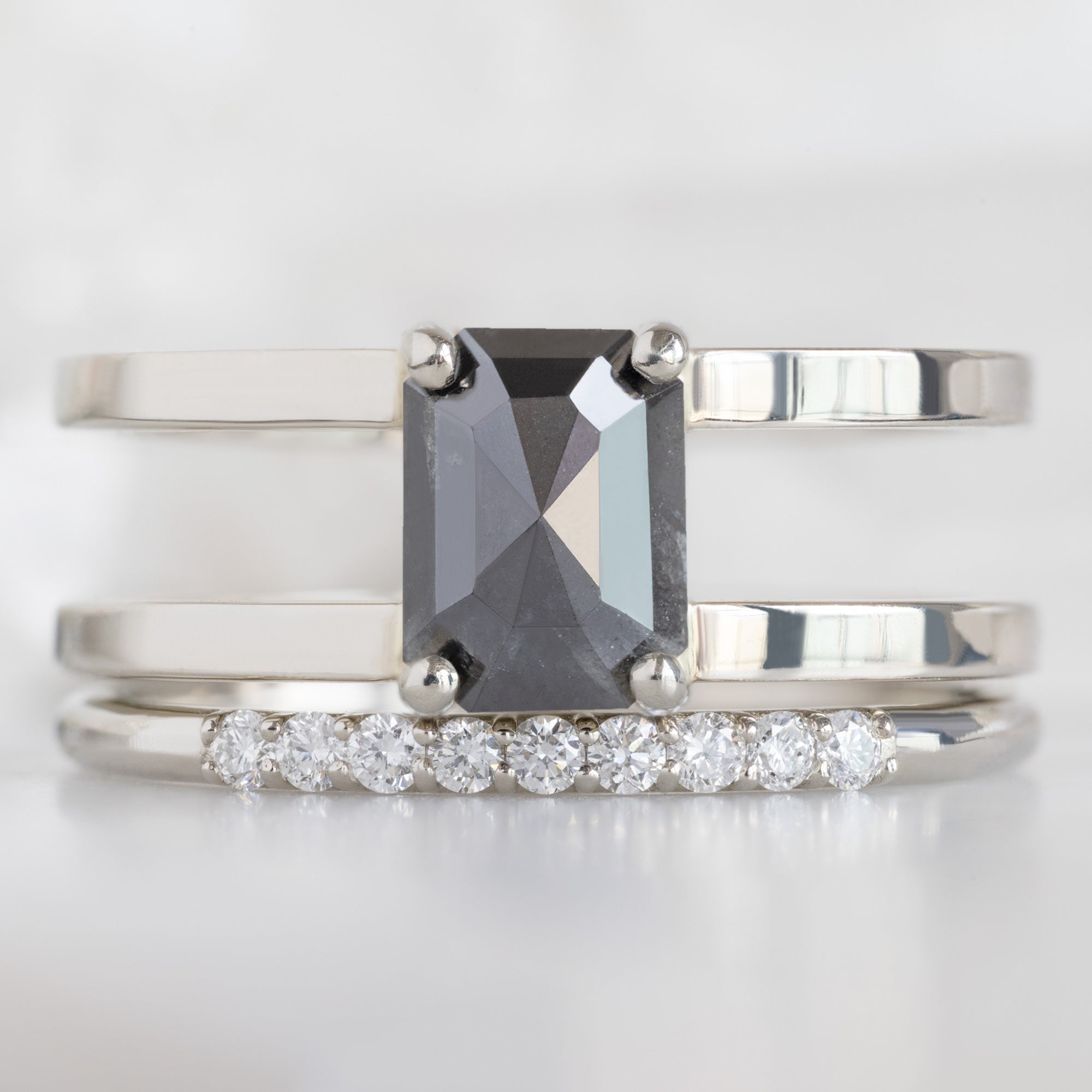 The Luxe White Diamond Pavé Wedding Band in 14K White Gold Stacked with Double Band Black Diamond Engagement Ring on White Marble