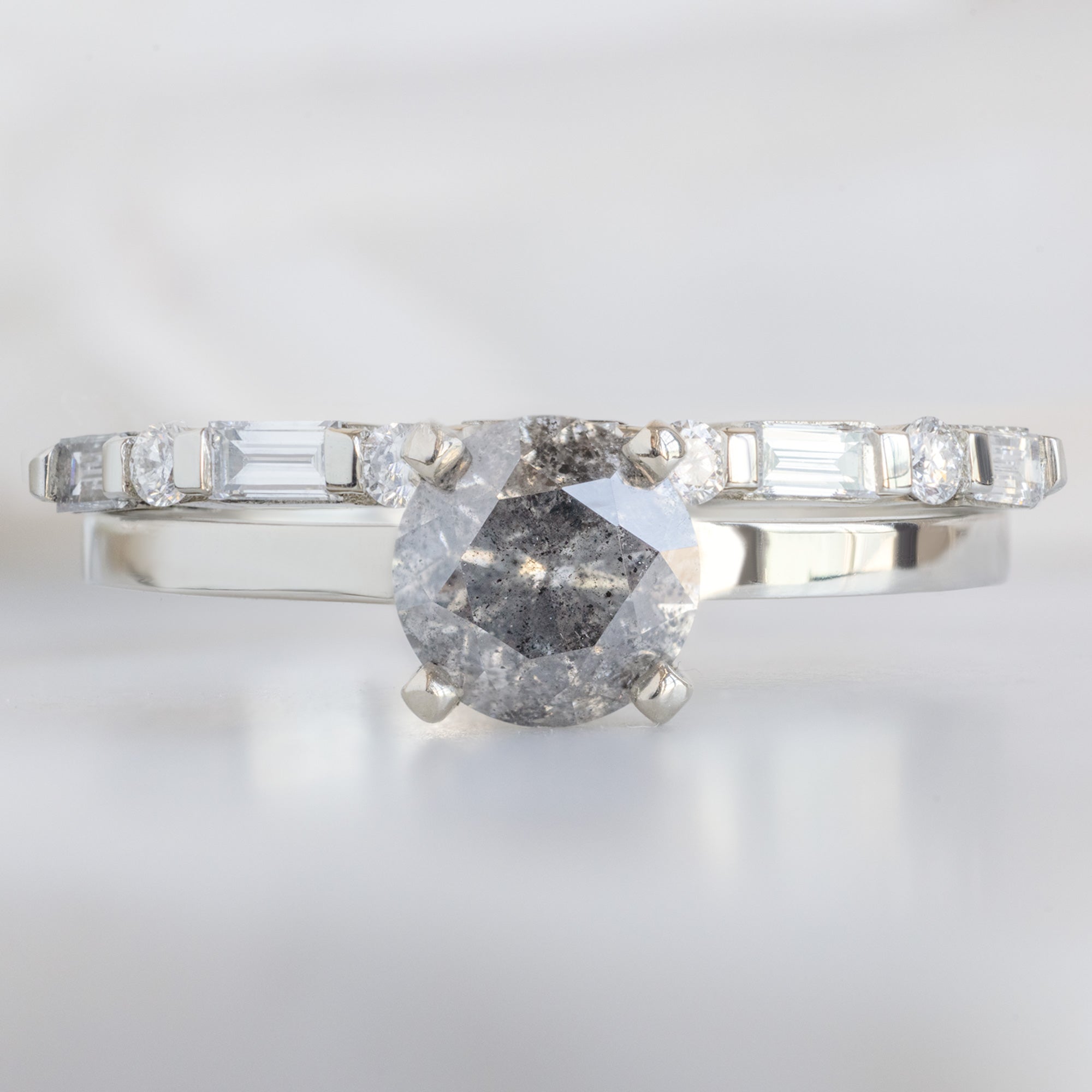 The Luxe Baguette White Diamond Eternity Band in 14K White Gold stacked with round salt and pepper diamond engagement ring on white marble surface