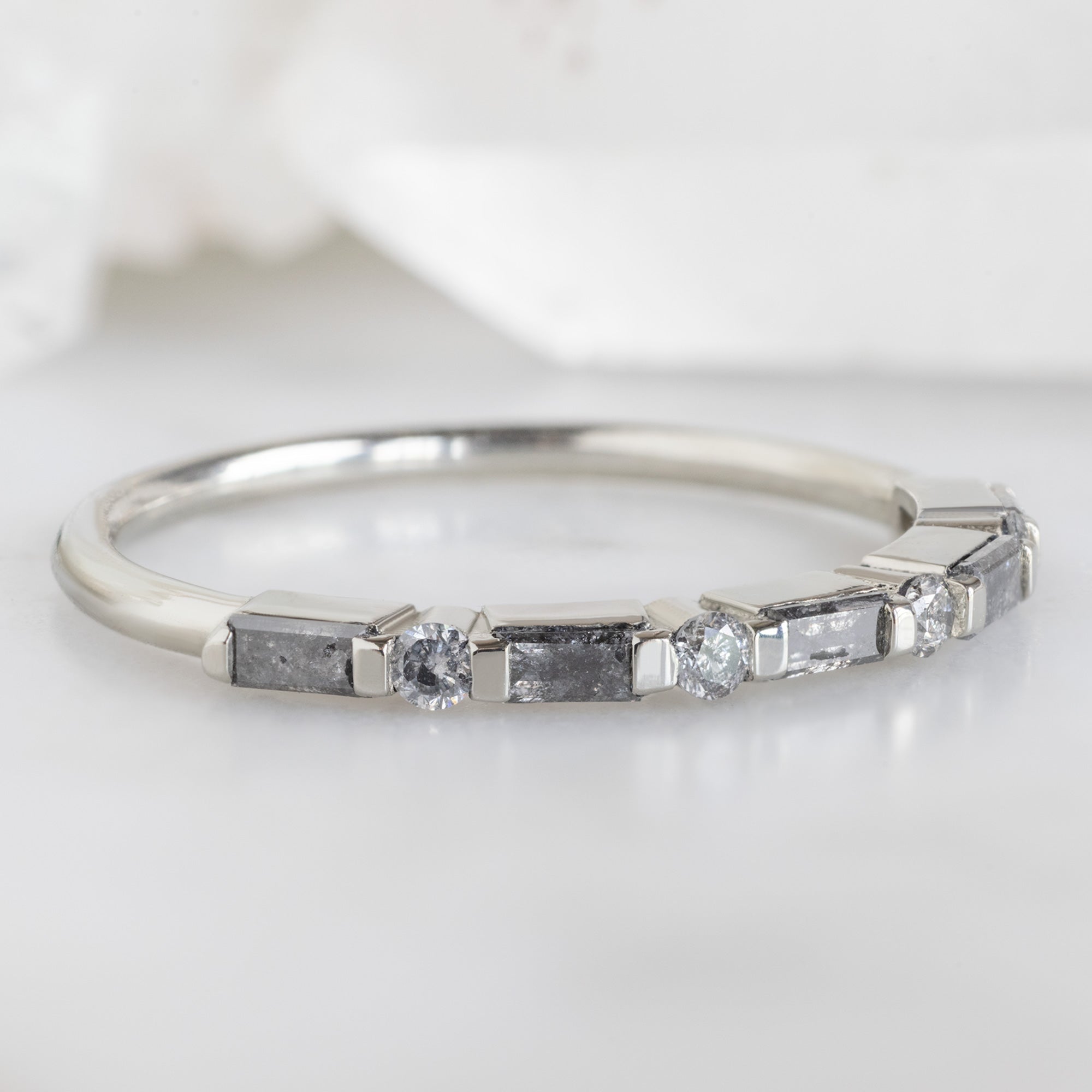 The Luxe Baguette Salt and Pepper Diamond Eternity Band in 14K White Gold on White Marble Surface