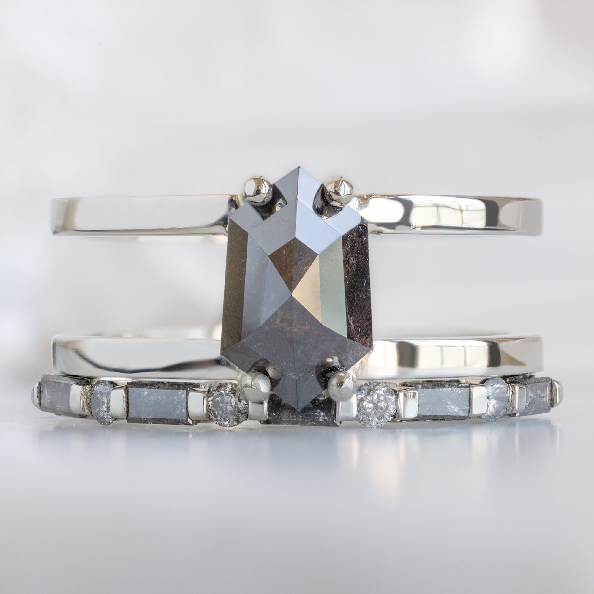 The Luxe Baguette Salt and Pepper Diamond Eternity Band in 14K White Gold stacked with double banded salt and pepper diamond engagement ring on white marble surface