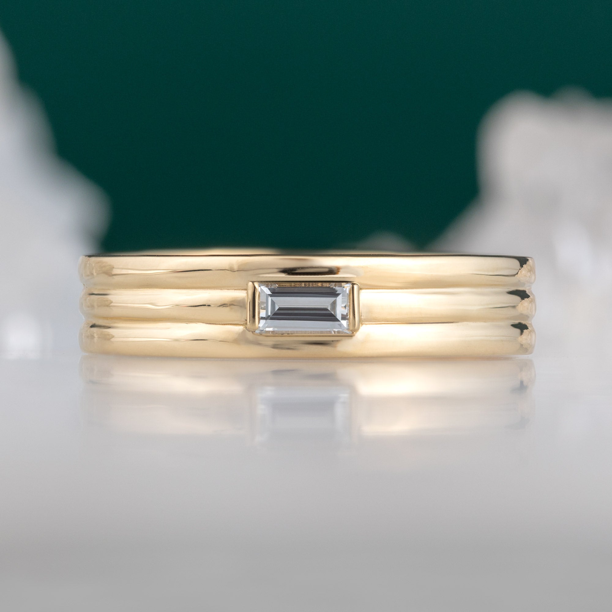The Men's Stratum Band with a Lab Grown Baguette in 18K Yellow Gold on White Marble with Green Background