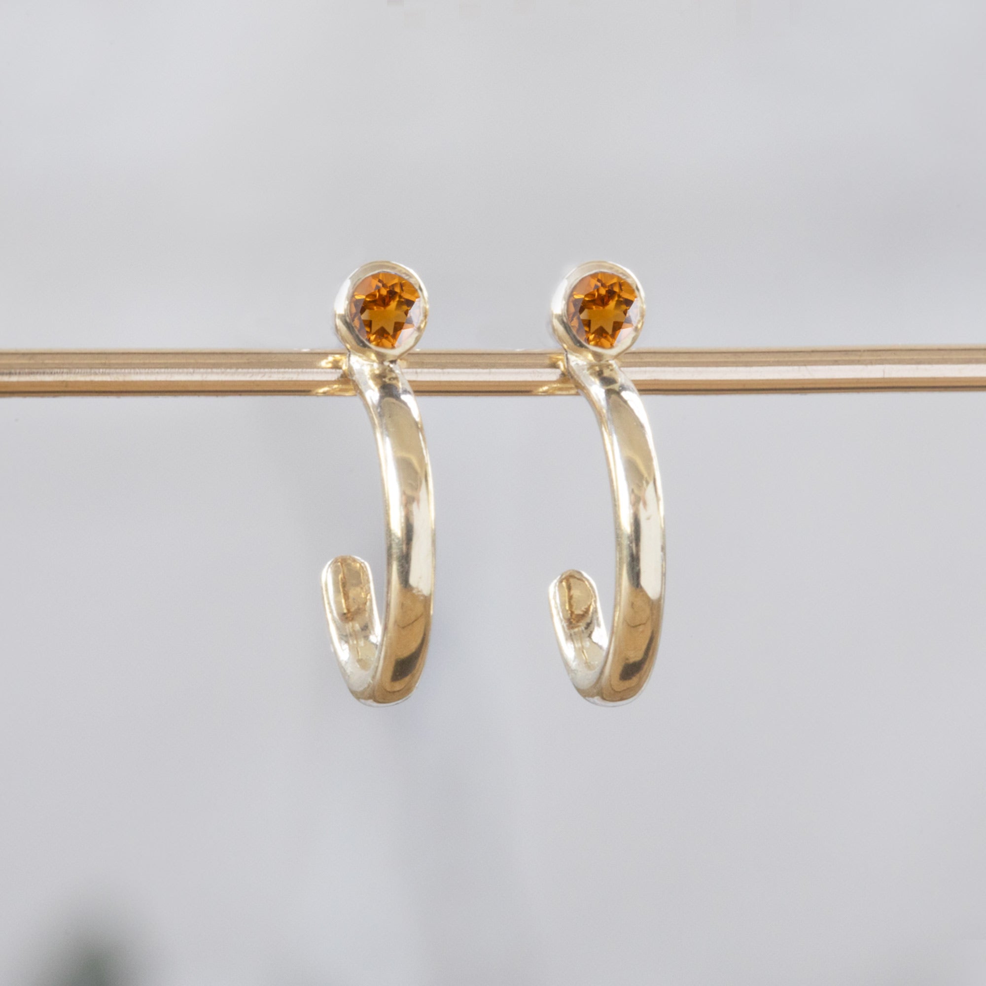 Custom Citrine Birthstone Hoop Earrings | 14K Yellow Gold displayed on holding bar with white blurred background. 
