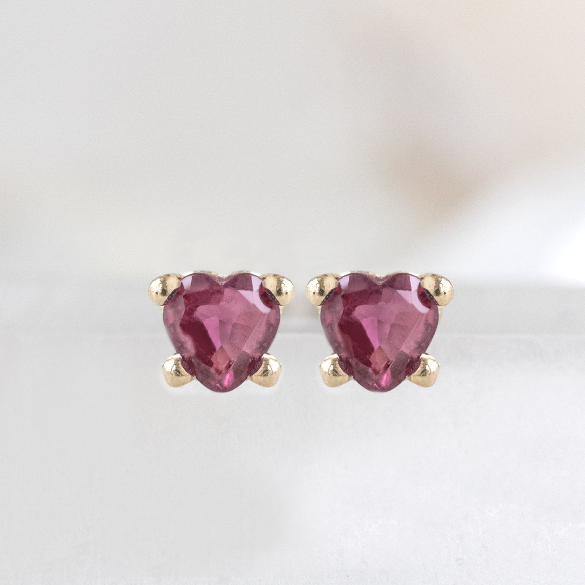The Teensy Ruby Heart Studs in 14K Yellow Gold on White Marble