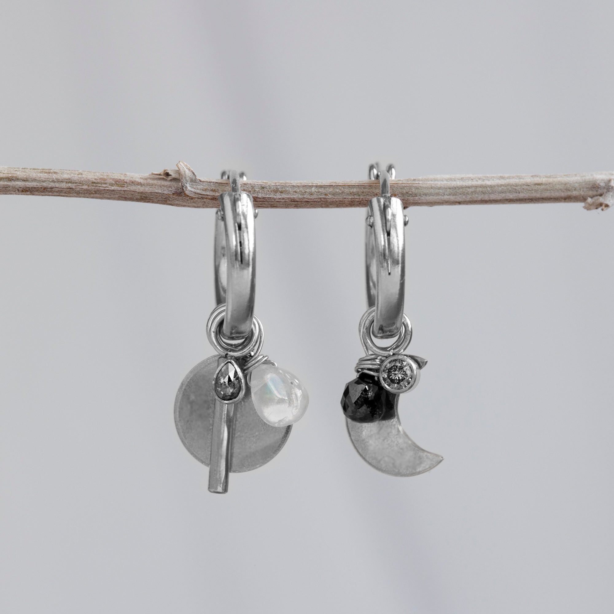 Custom Charm Hoop Earrings | Sterling Silver displayed on holding bar with grey background. 
