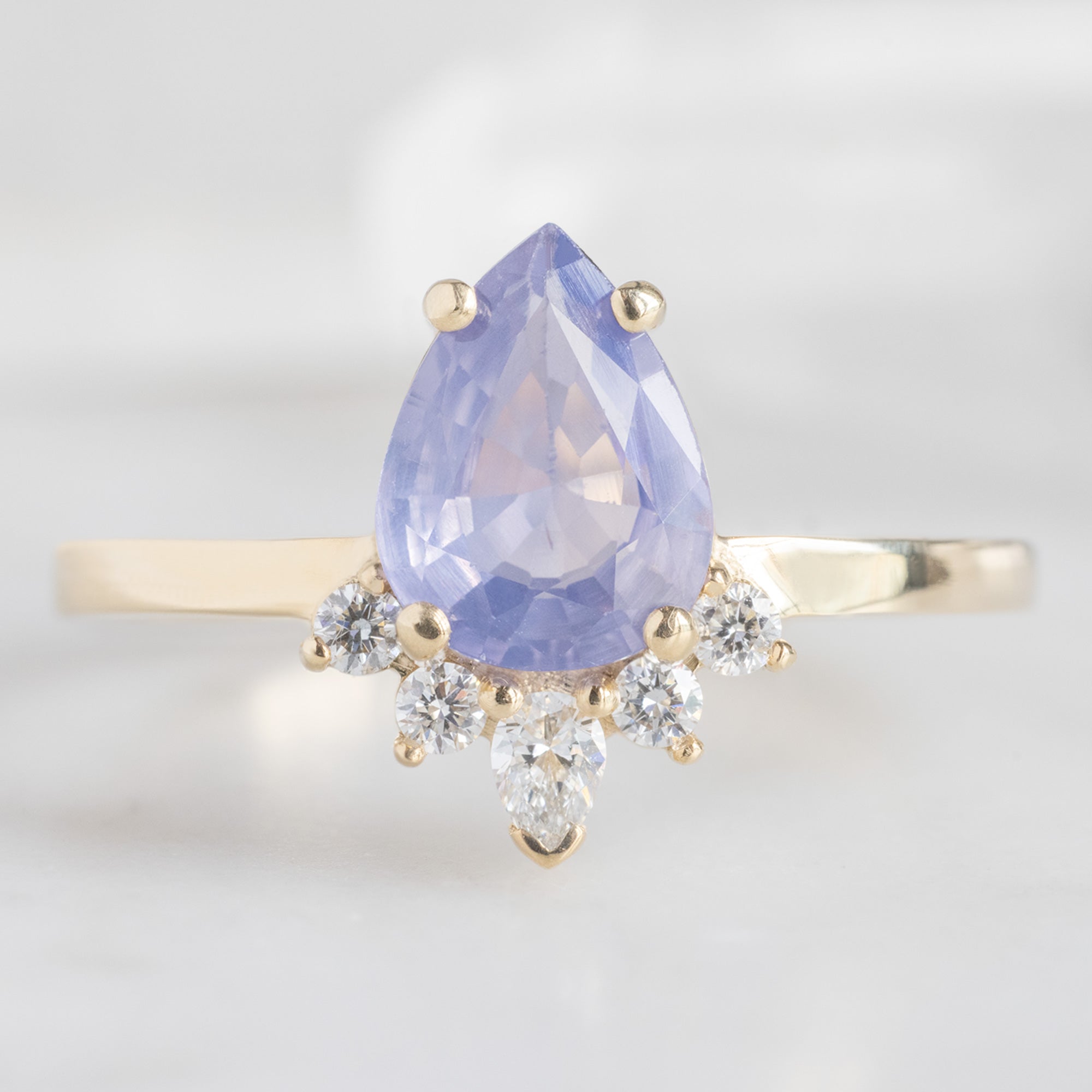 The Aster Ring | 1.23 carat Pear Cut Lavender Sapphire in 14K Yellow Gold with white blurred background. 