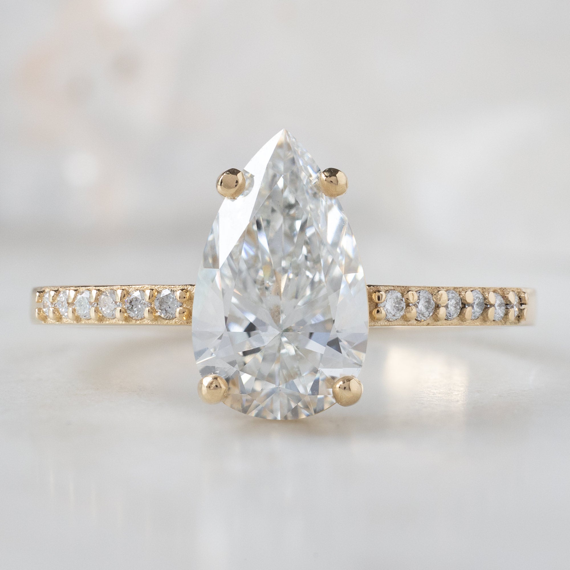The Willow Ring with a Lab Grown Pear White Diamond in 14K Yellow Gold on White Marble