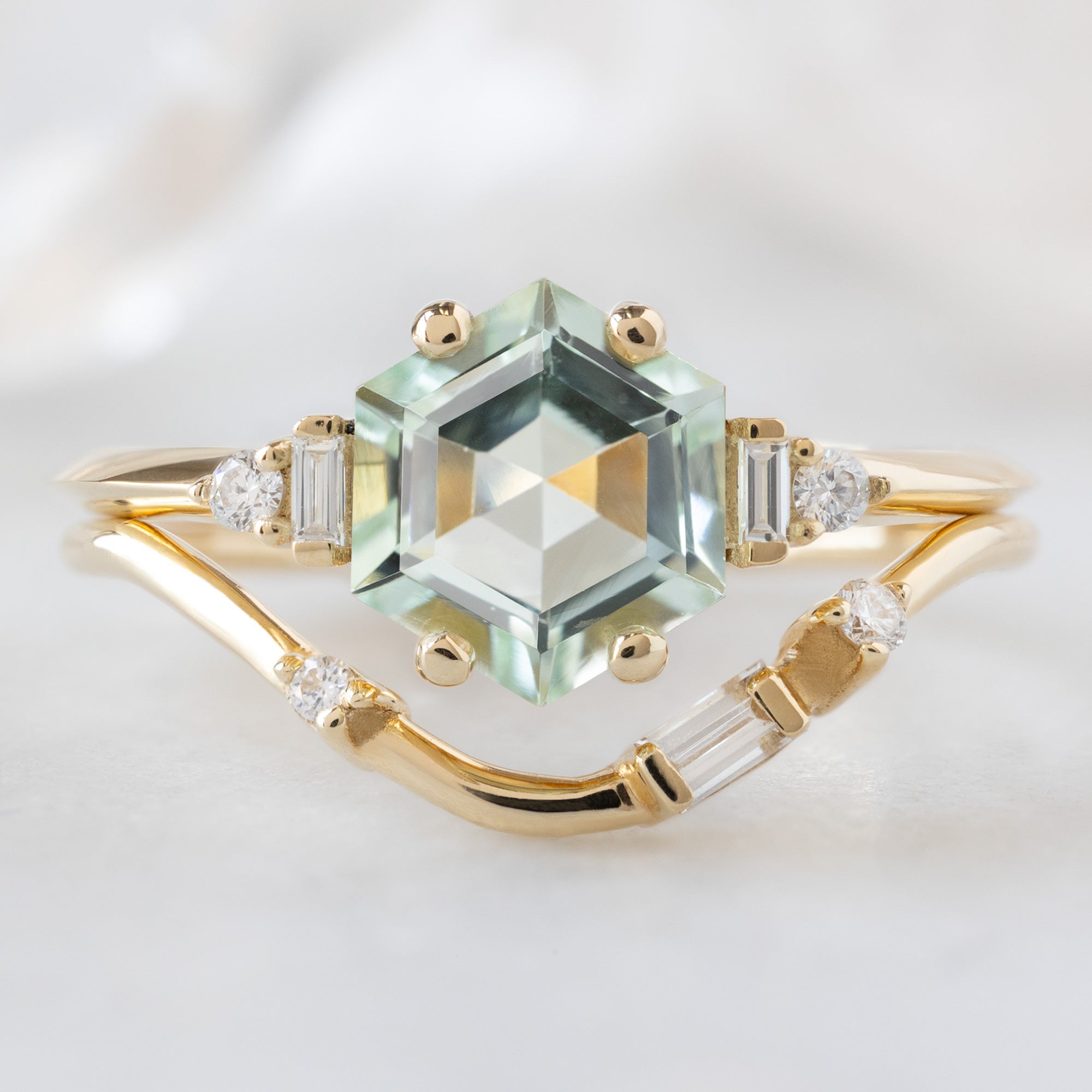 The Primrose Ring with a 1.05ct Hexagon Tourmaline in 14K Yellow Gold  Stacked with the Asymmetrical Baguette Arc Stacking Band on White Marble Surface