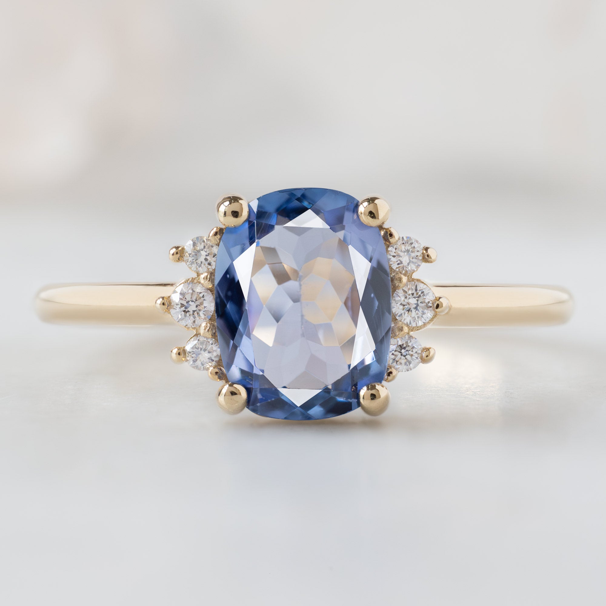 The Sunflower Ring with a 1.02ct Cushion Cut Tanzanite in 14K Yellow Gold on White Marble Surface