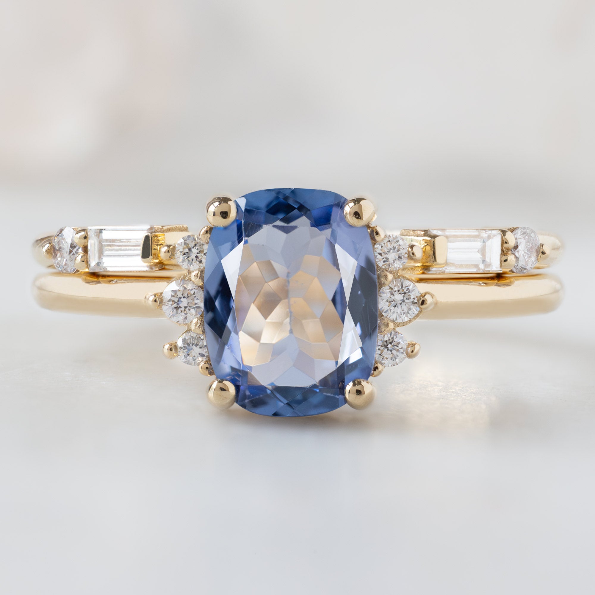 The Sunflower Ring with a 1.02ct Cushion Cut Tanzanite in 14K Yellow Gold on Stacked with the Open Cuff Luxe Baguette Diamond Stacking Ring on White Marble Surface