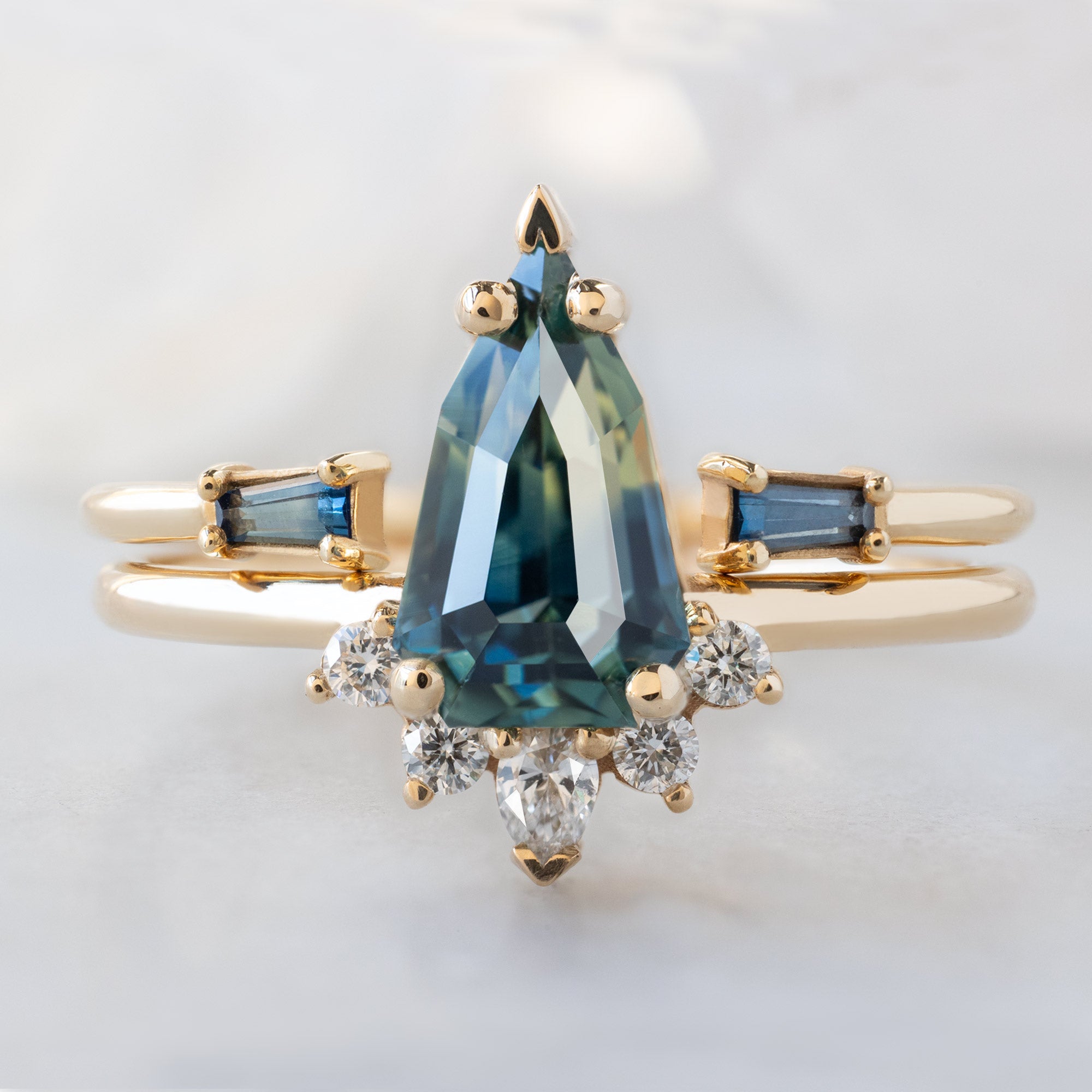 The Aster Ring with a 1.56ct Geometric Montana Parti Sapphire in 14K Yellow Gold Stacked with the Open Cuff Sapphire Baguette Stacking Band on White Marble Surface