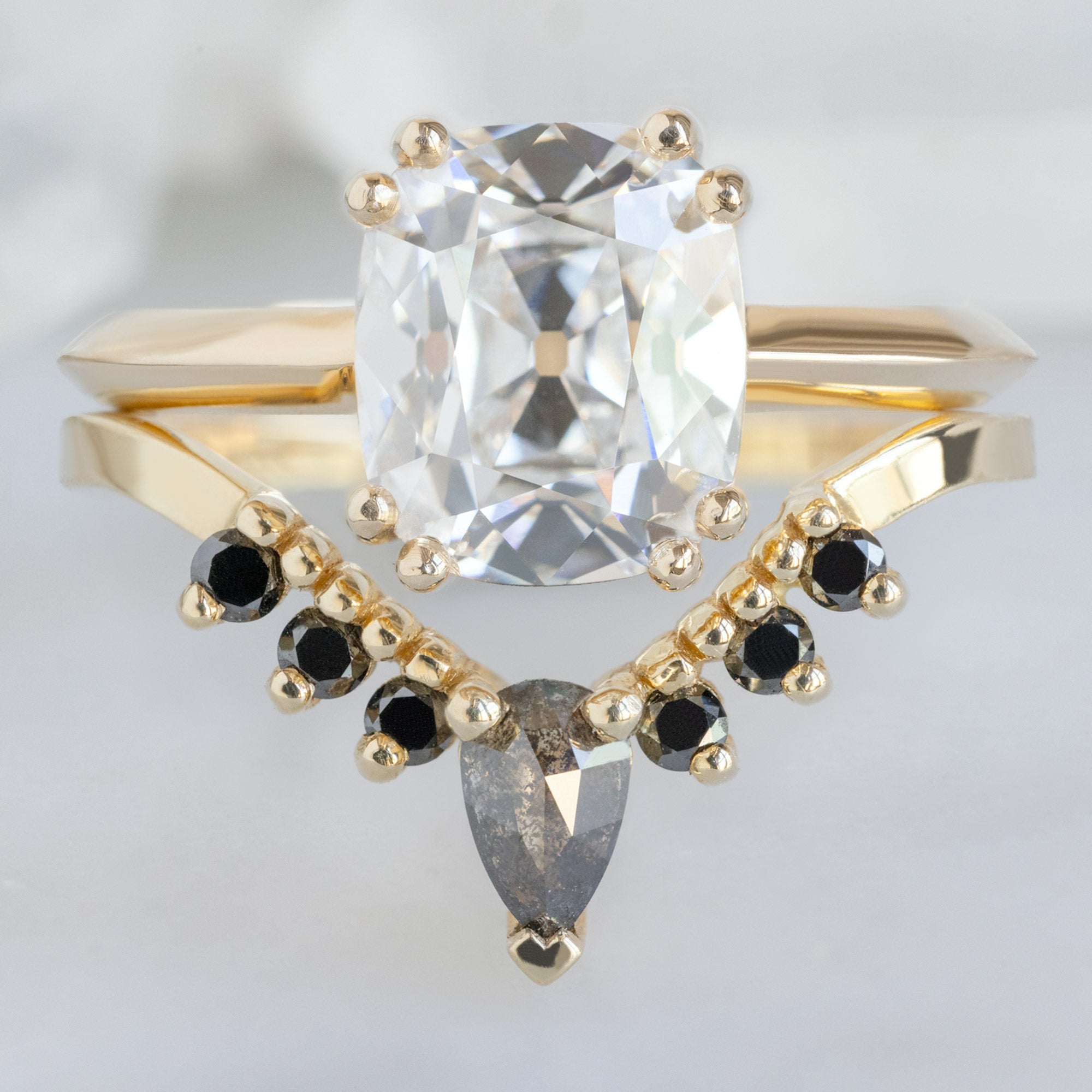The Bryn Ring with a 2.04ct Old Mine Cut Lab Grown White Diamond in 14K Yellow Gold Stacked with the Black Diamond Sunburst Stacking Band on White Marble Surface
