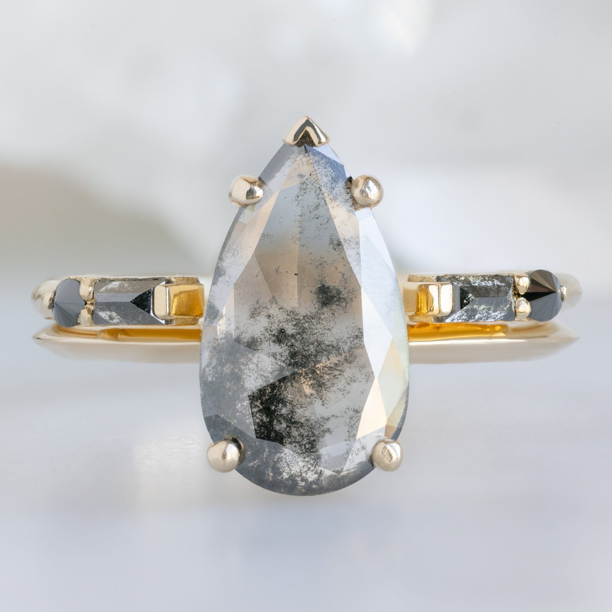 The Sage Ring with a 1.19ct Pear Lab Grown Salt and Pepper Diamond in 14K Yellow Gold Stacked with the Open Cuff Luxe Black Diamond Baguette Stacking Band on White Marble Surface