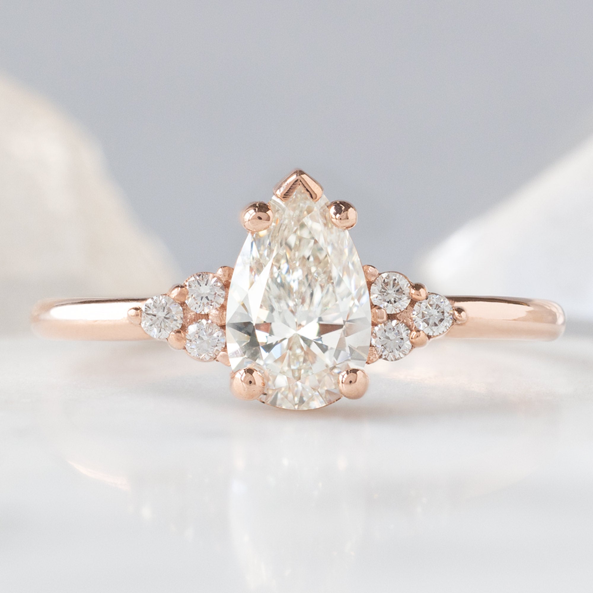 The Ivy Ring with a 0.65ct Pear White Diamond in 14K Rose Gold on White and Blue Background