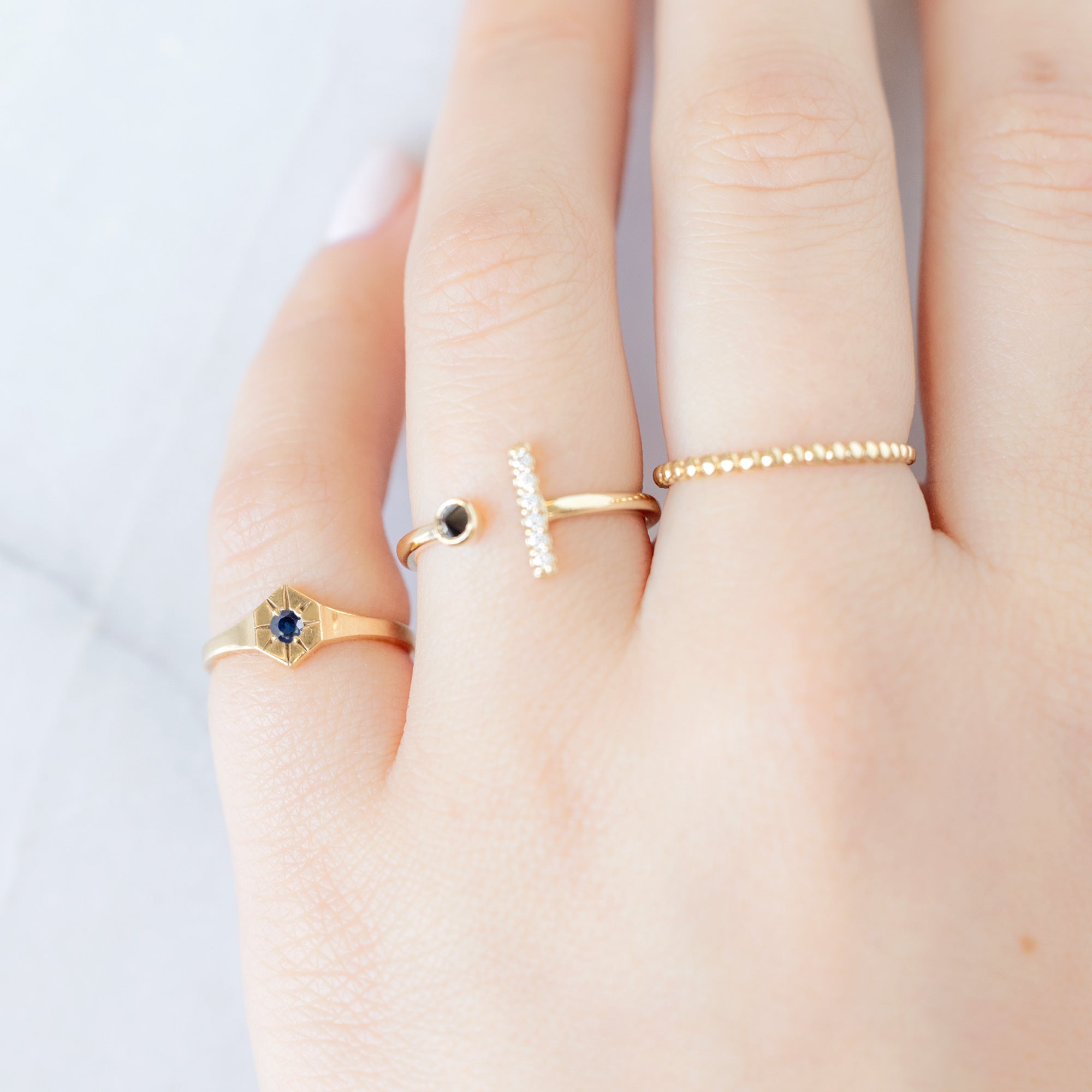Custom Blue Sapphire Birthstone Signet Ring | 10K Yellow Gold displayed on model's left hand pinky finger alongside two other rings on consecutive fingers. 