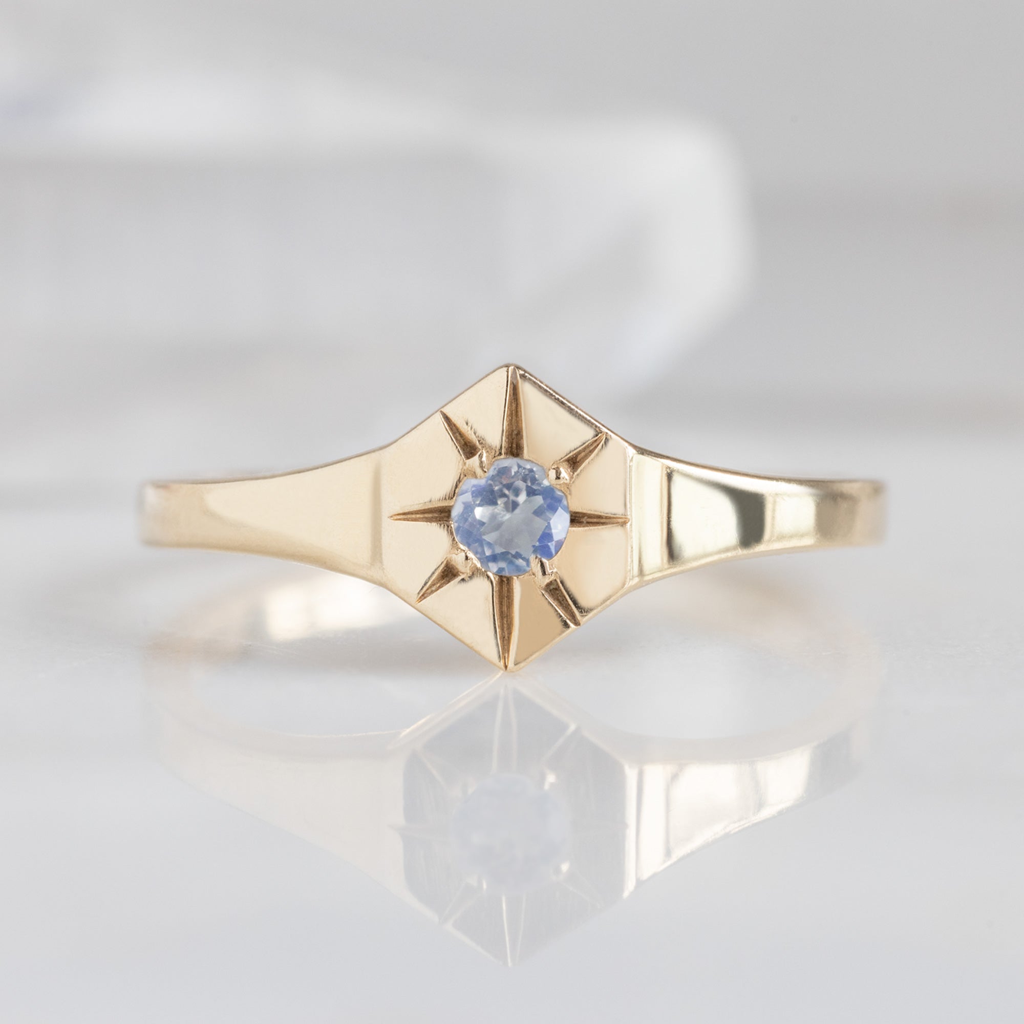 Custom Moonstone Birthstone Signet Ring | 10K Yellow Gold. Displayed on marble surface with white blurred background. 