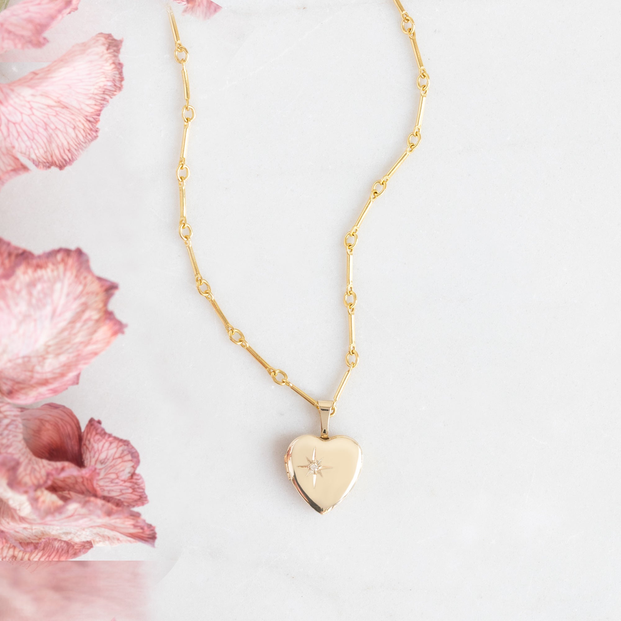 The Sweetheart Diamond Locket Necklace in Yellow Gold on white background with pink flowers