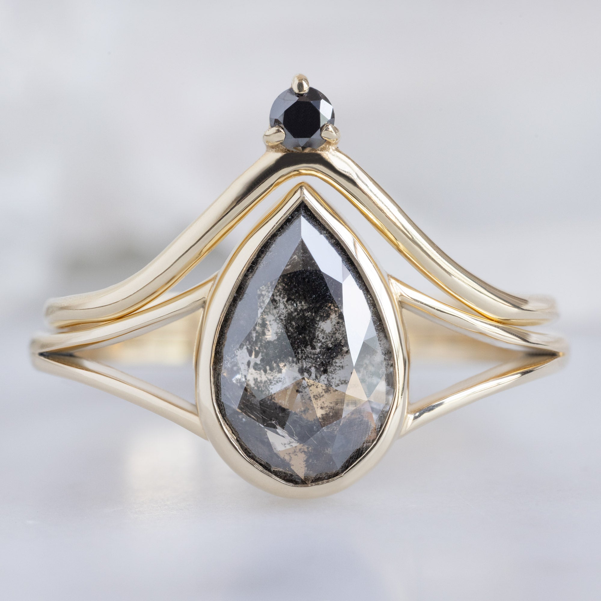 Black Diamond Crown Stacking Band in 14K Yellow Gold on White Marble Stacked with a Black Pear Diamond Engagement Ring
