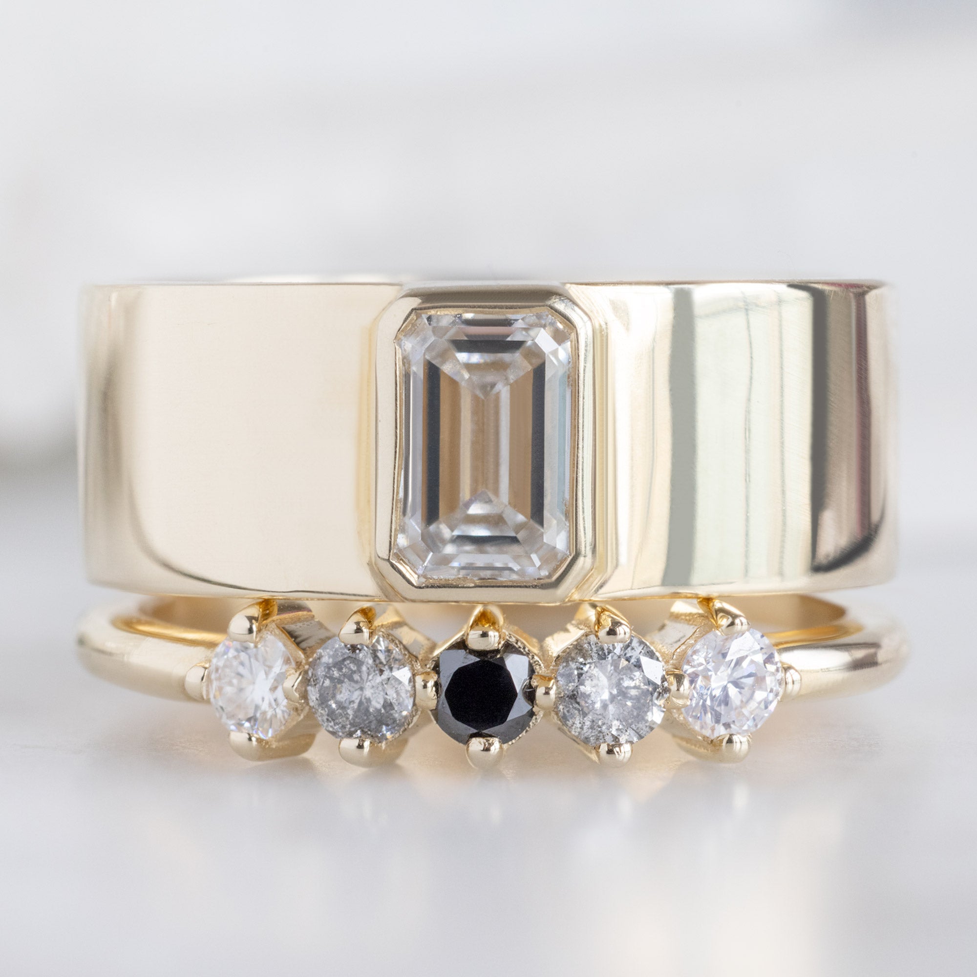 The Sequent Ombré Diamond Wedding Band in 14K Yellow Gold Stacked with White Diamond Cigar Band Engagement Ring on White Marble