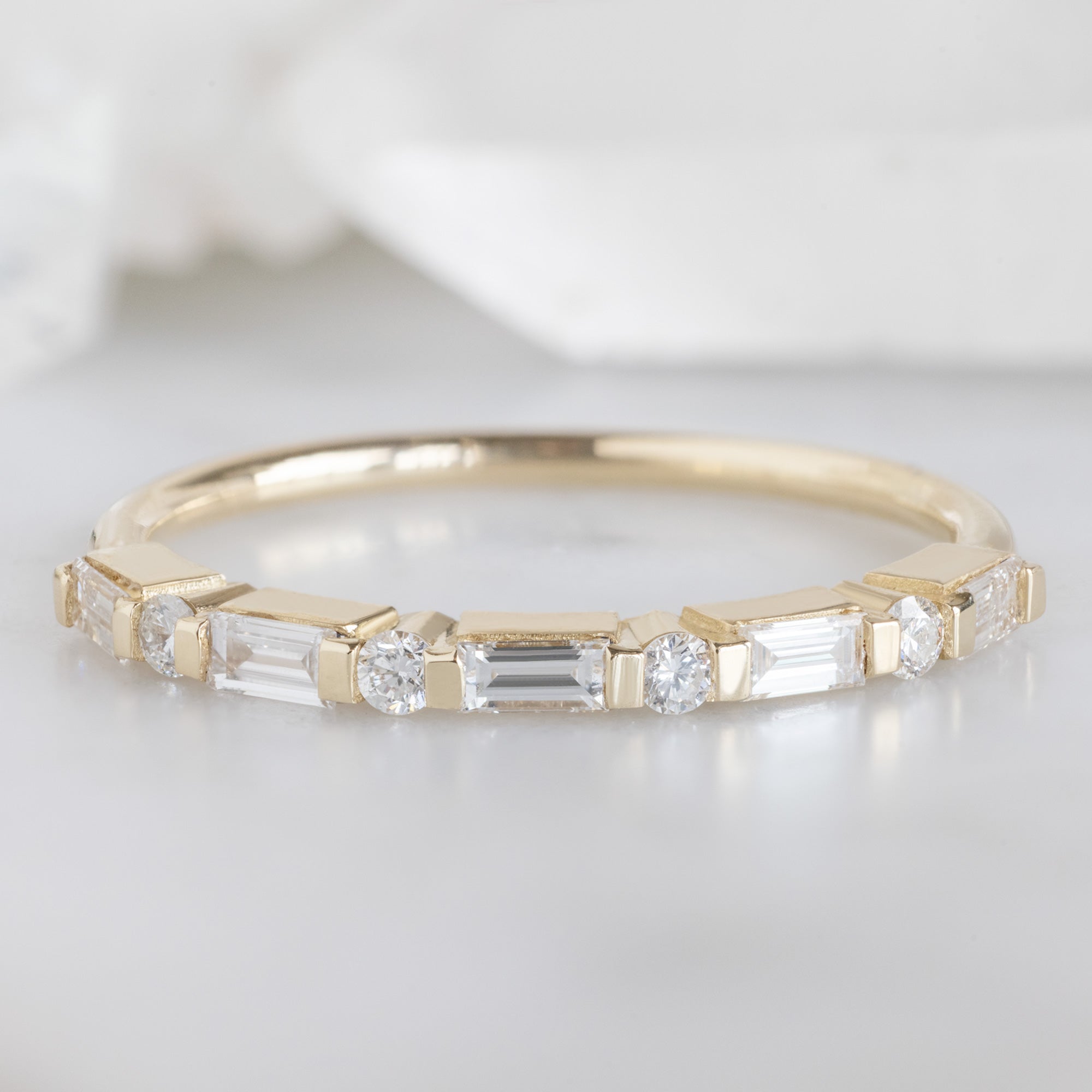 The Luxe Baguette White Diamond Eternity Band in 14K Yellow Gold on White Marble Surface
