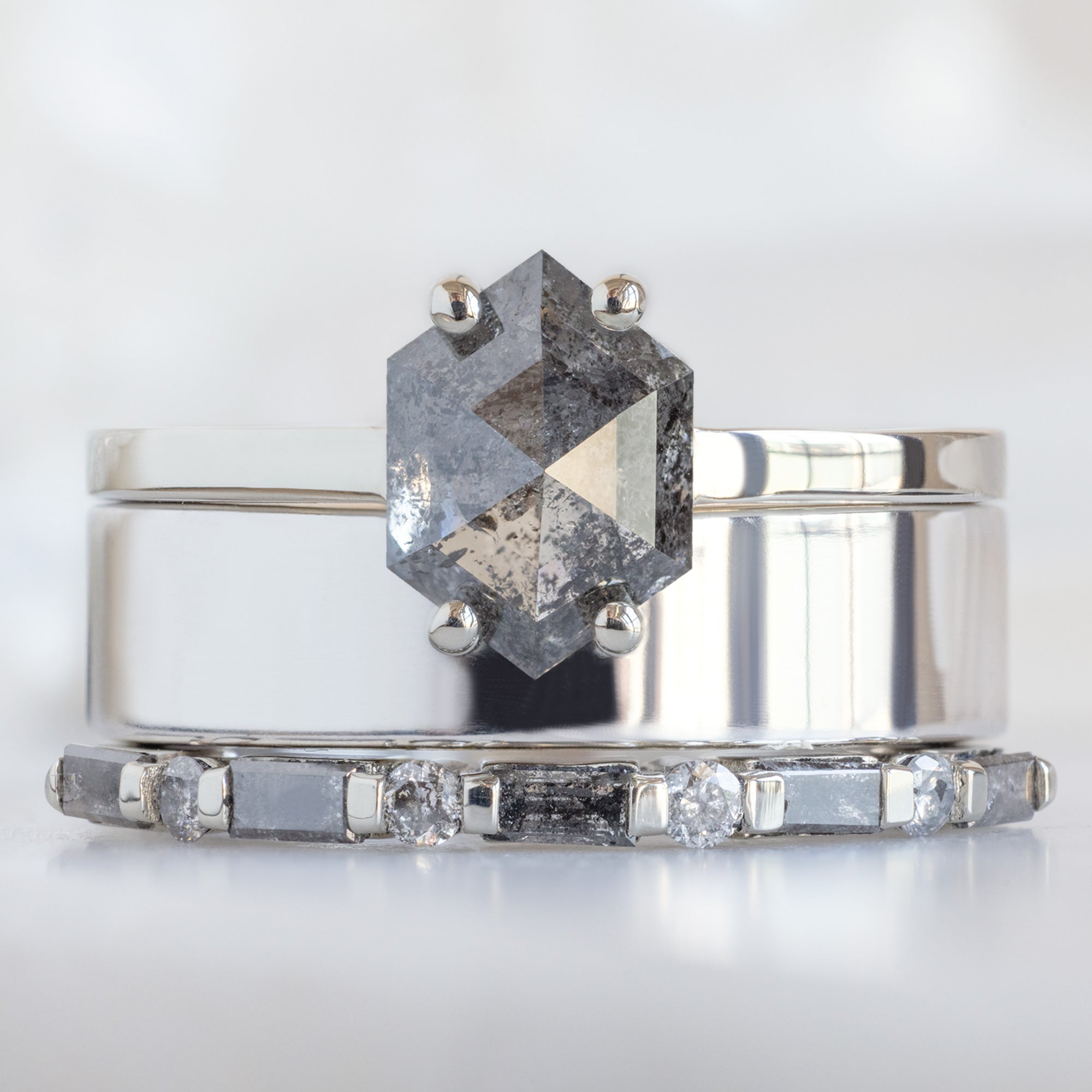 The Luxe Baguette Salt and Pepper Diamond Eternity Band in 14K White Gold stacked with hexagon salt and pepper diamond engagement ring on white marble surface